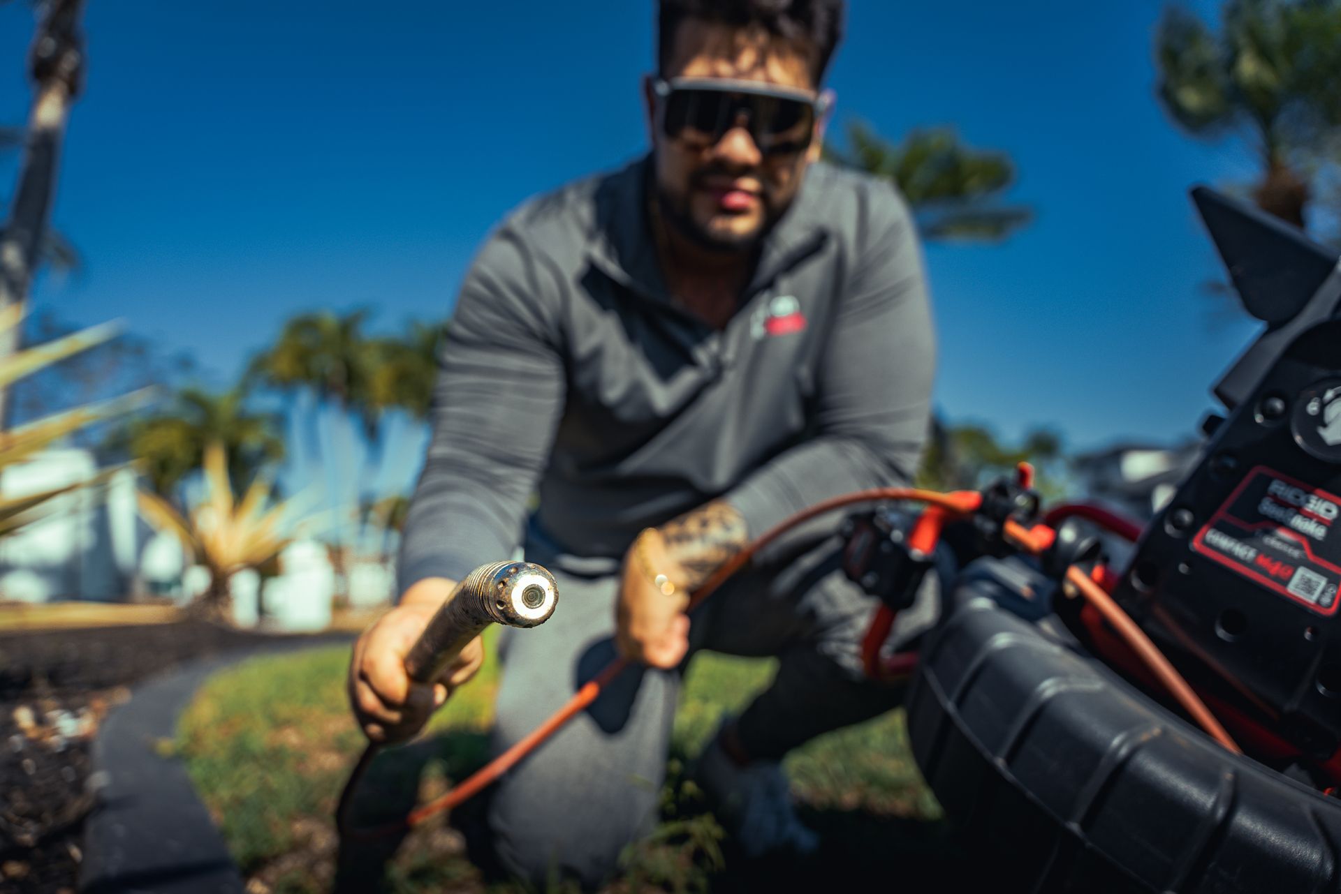 A man is kneeling down while holding a pipe and a camera.