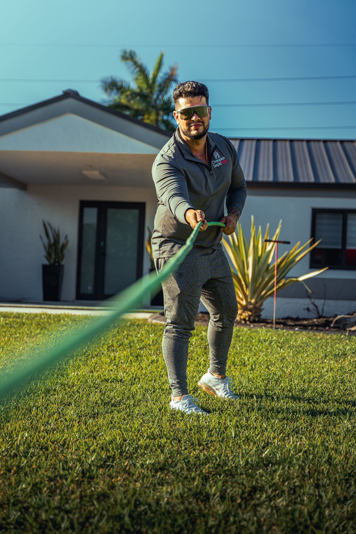 A man is holding a green hose in front of a house.