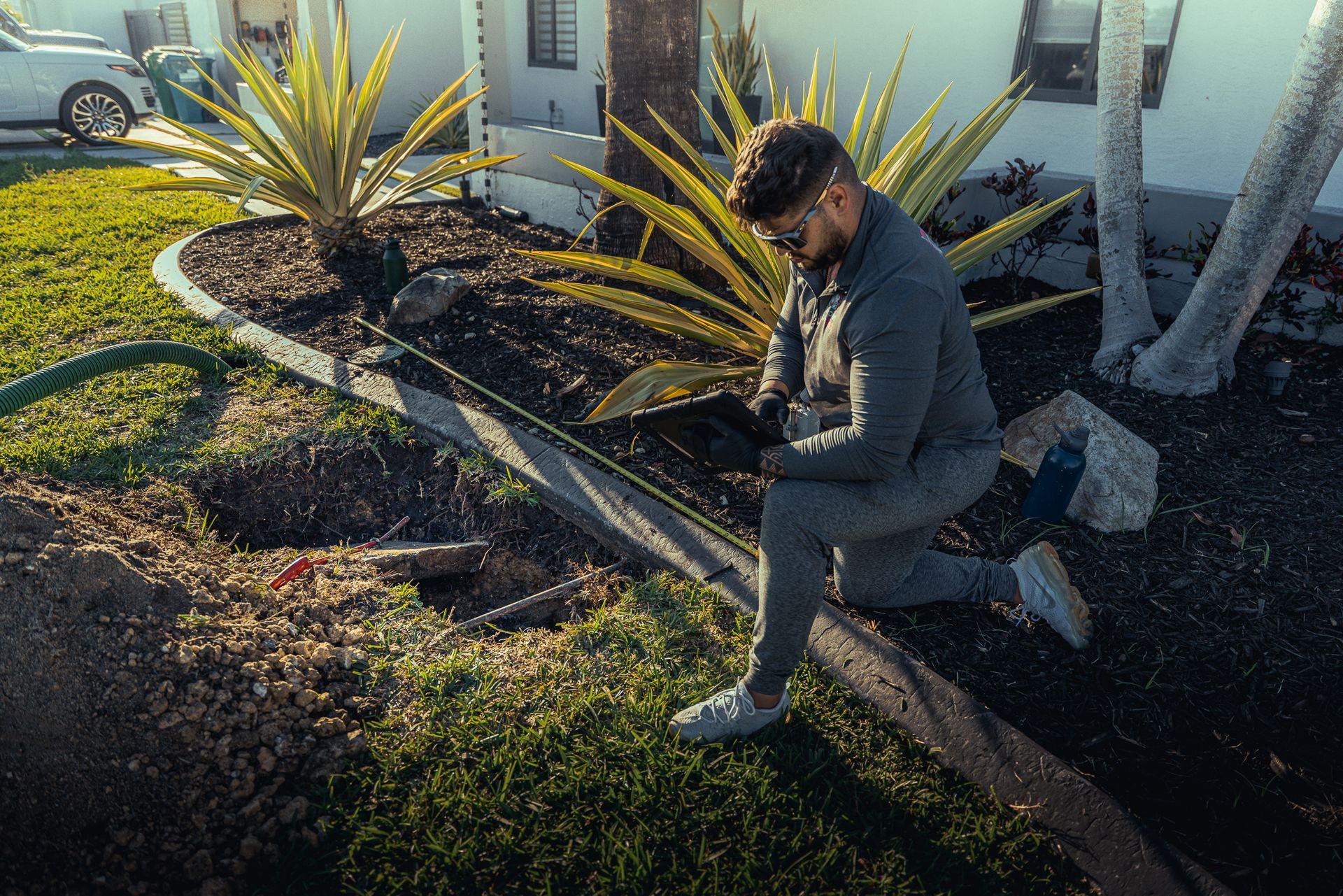 A man is kneeling down in front of a house looking at a tablet.