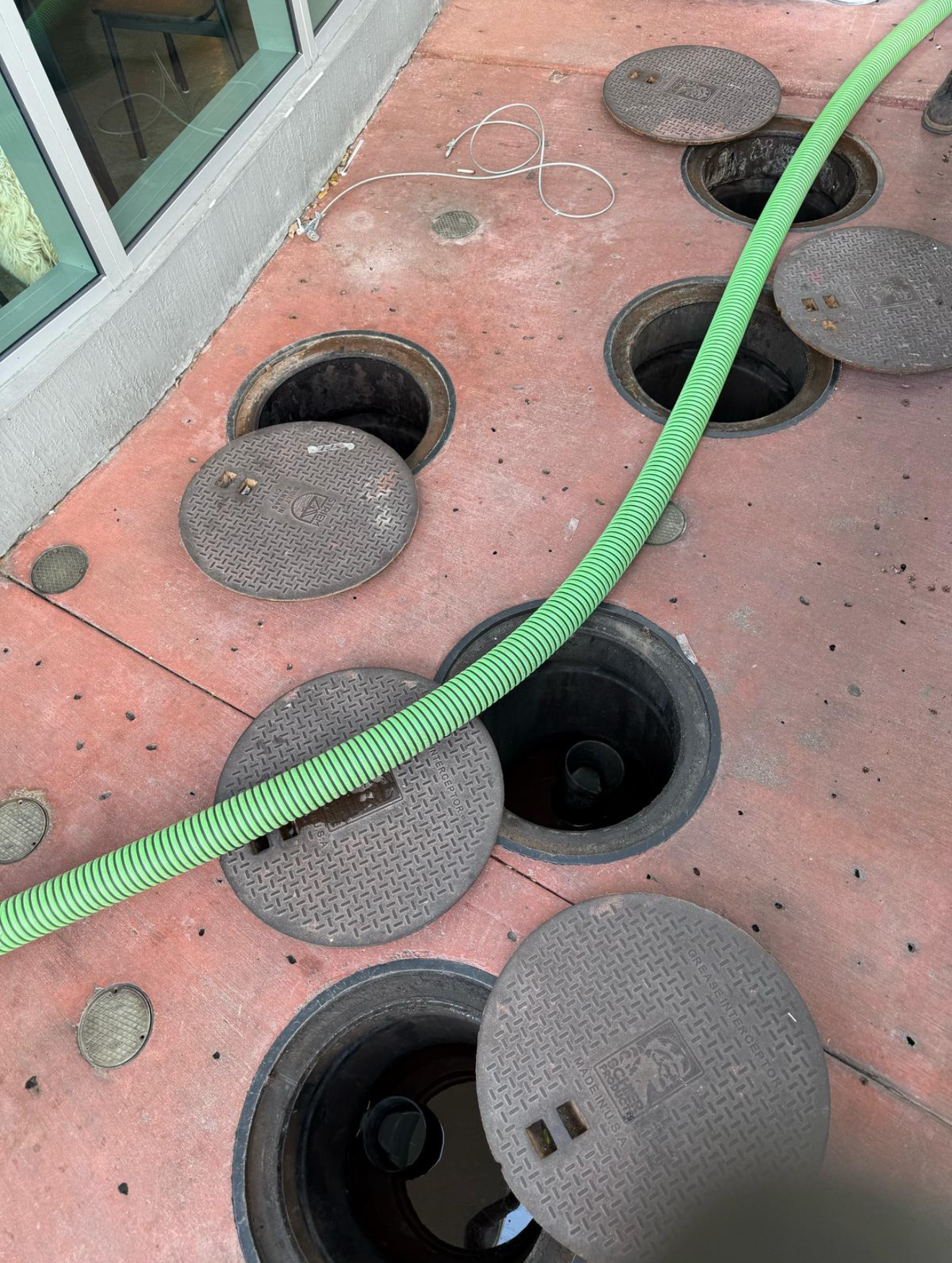 A green hose is connected to a group of manhole covers.