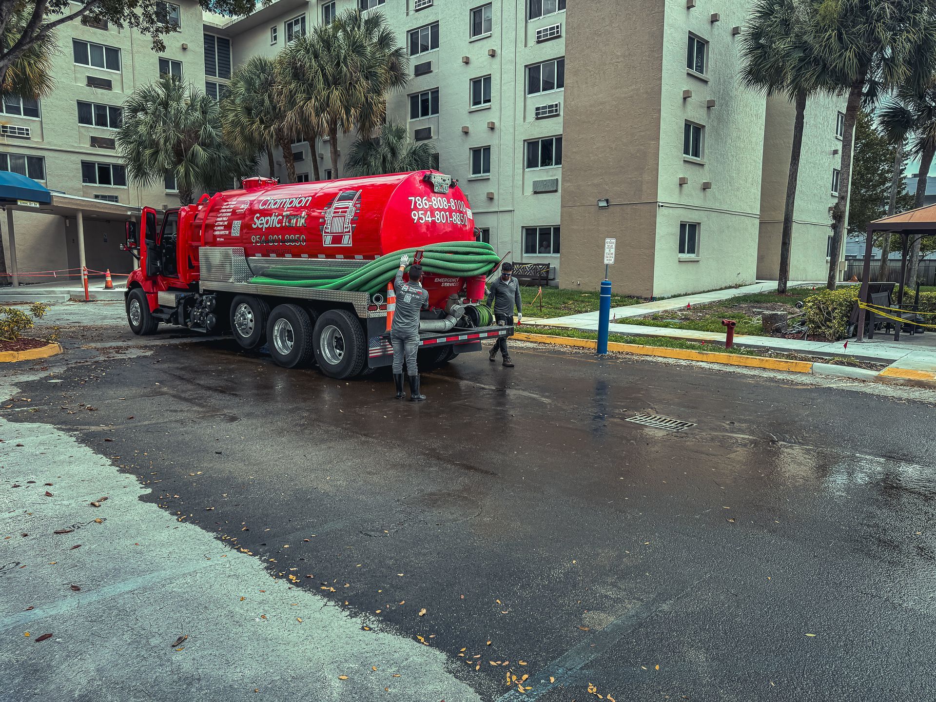 A red vacuum truck is parked on the side of the road in front of a building.