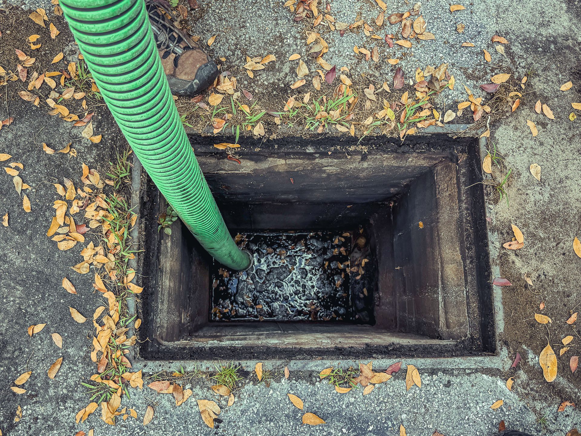 A green hose is being used to pump water into a manhole.