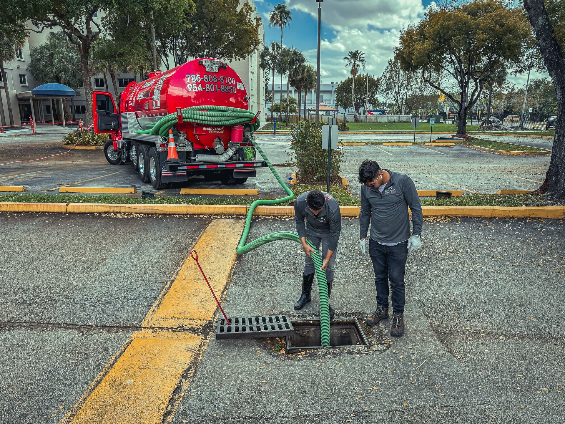 Two men are working on a manhole cover in a parking lot.
