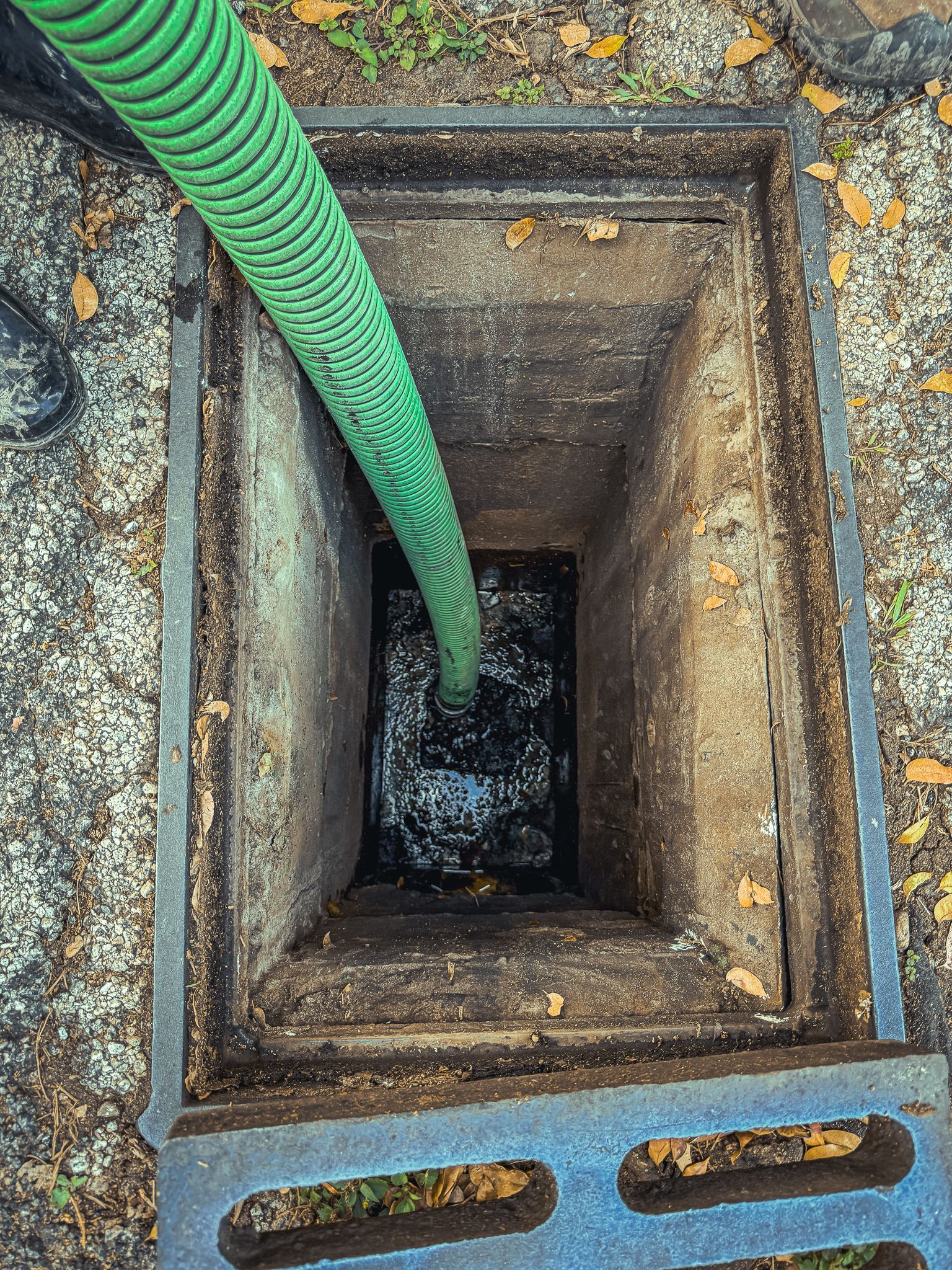 A green hose is being used to pump water into a manhole cover.