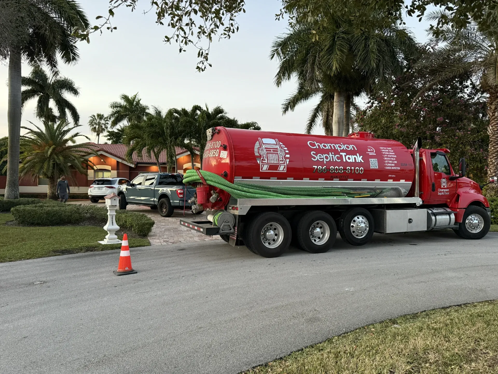 A red septic tank truck is parked in the driveway of a house.