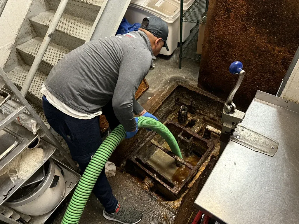 A man is using a green hose to clean a drain in a kitchen.