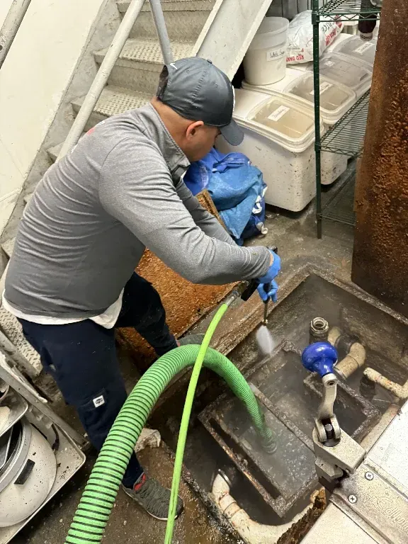 A man is cleaning a drain with a green hose.