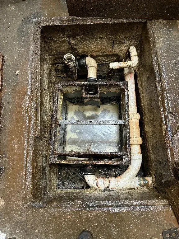 A dirty drain with pipes coming out of it.