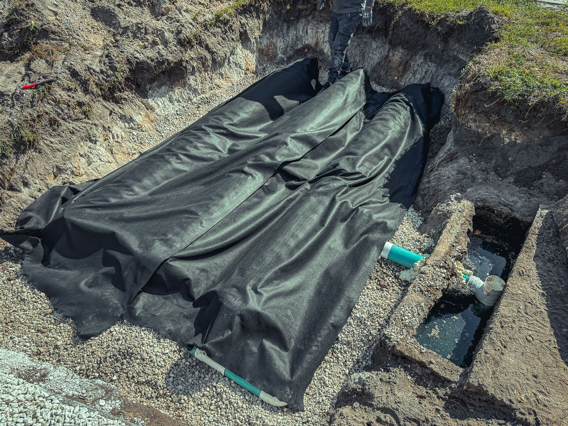 A black tarp is laying in the dirt next to a pipe.
