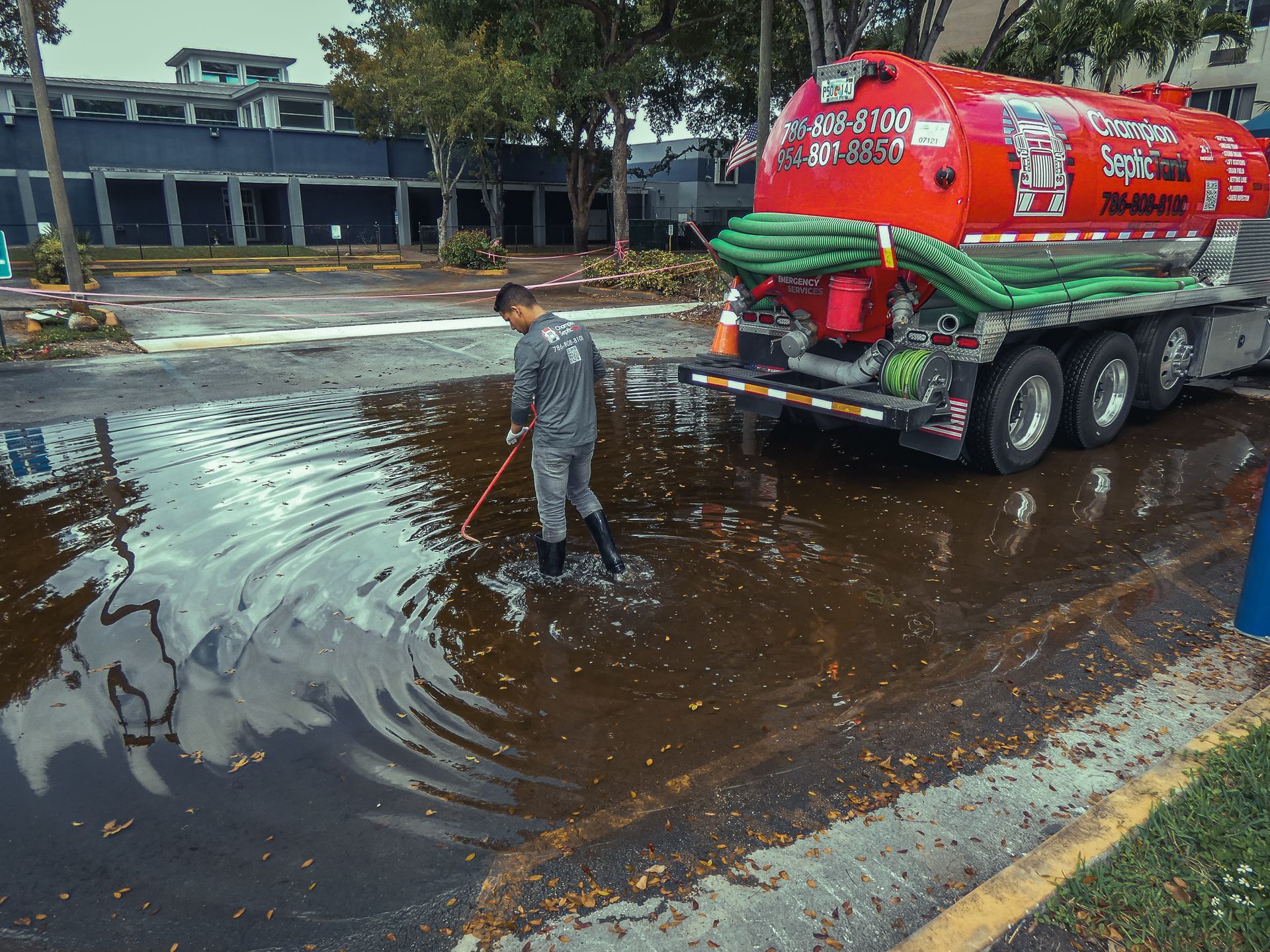 A man is standing in a puddle of water next to a vacuum truck.
