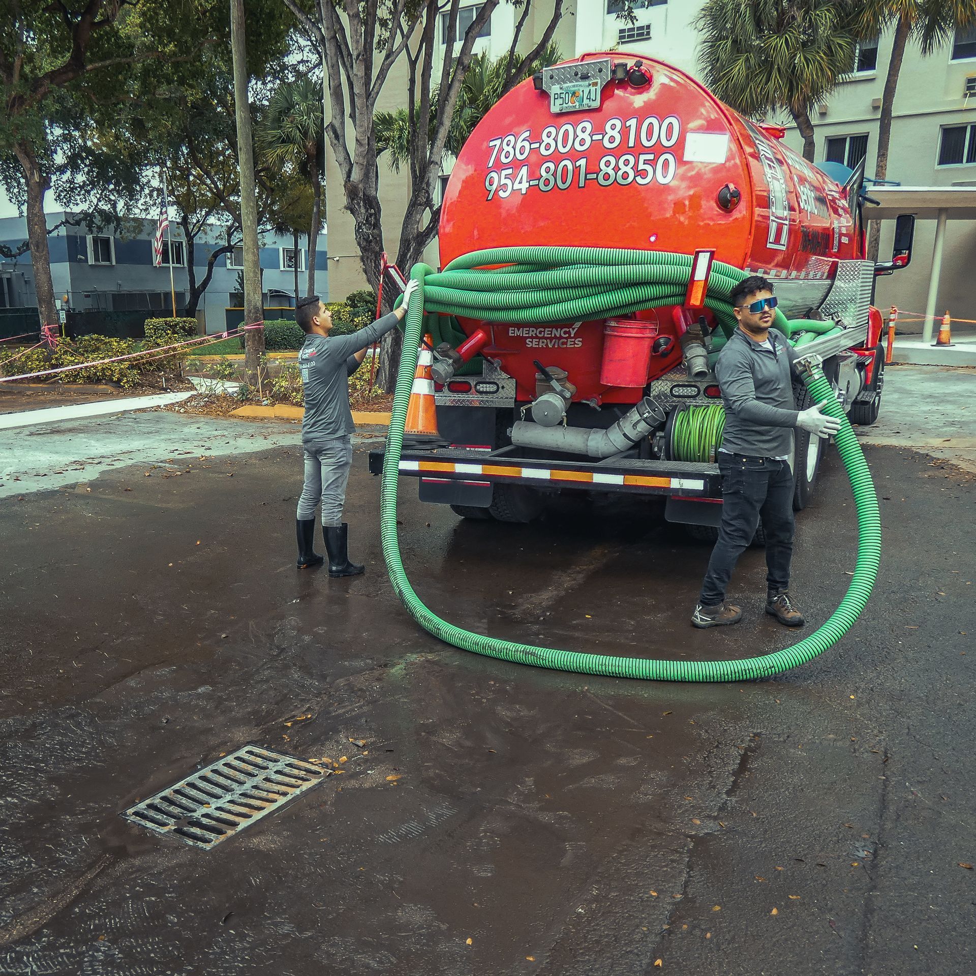 A man is holding a large green hose in front of a septic tank