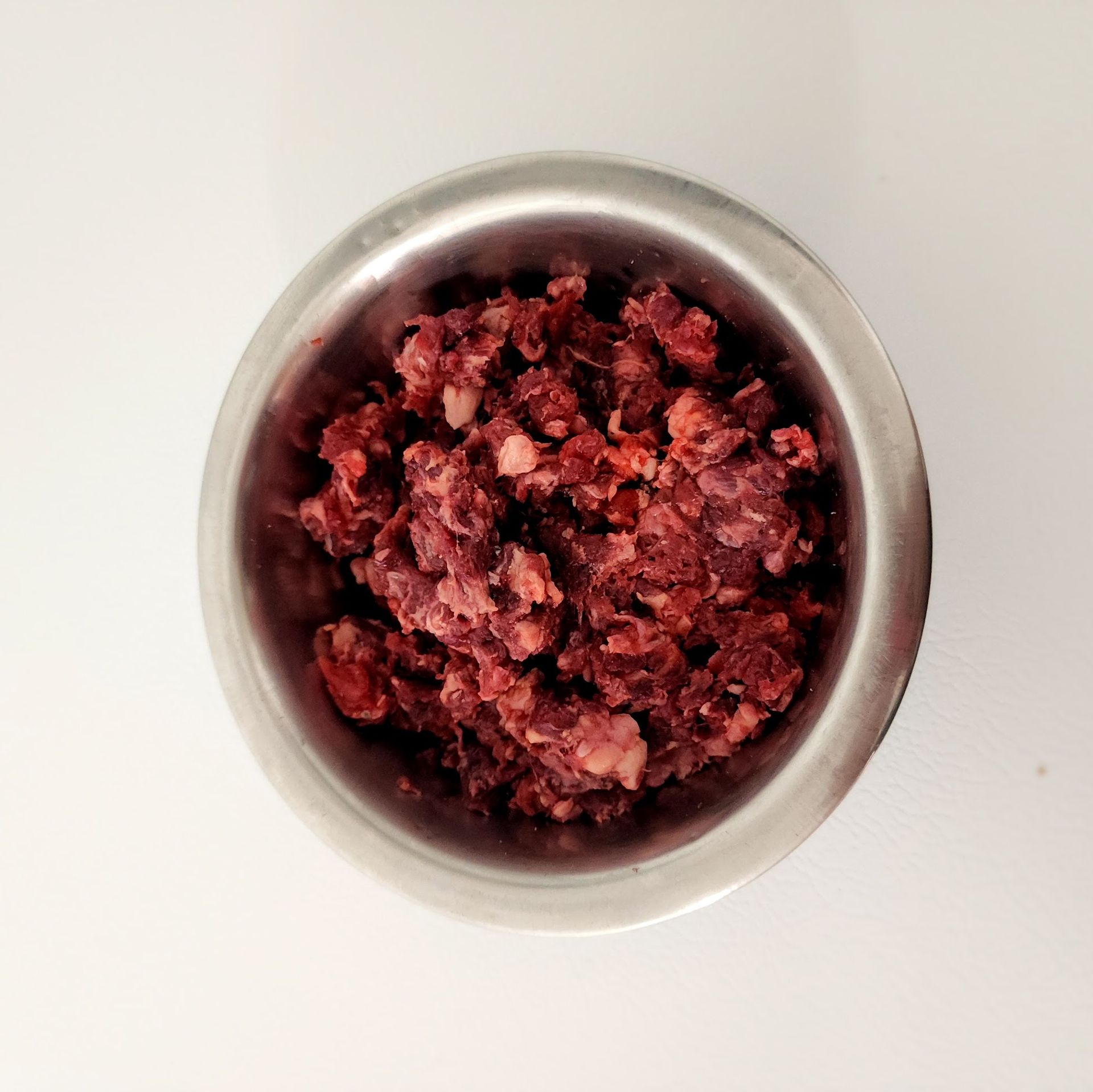 Ground meat in a metal bowl, top-down view on white background.