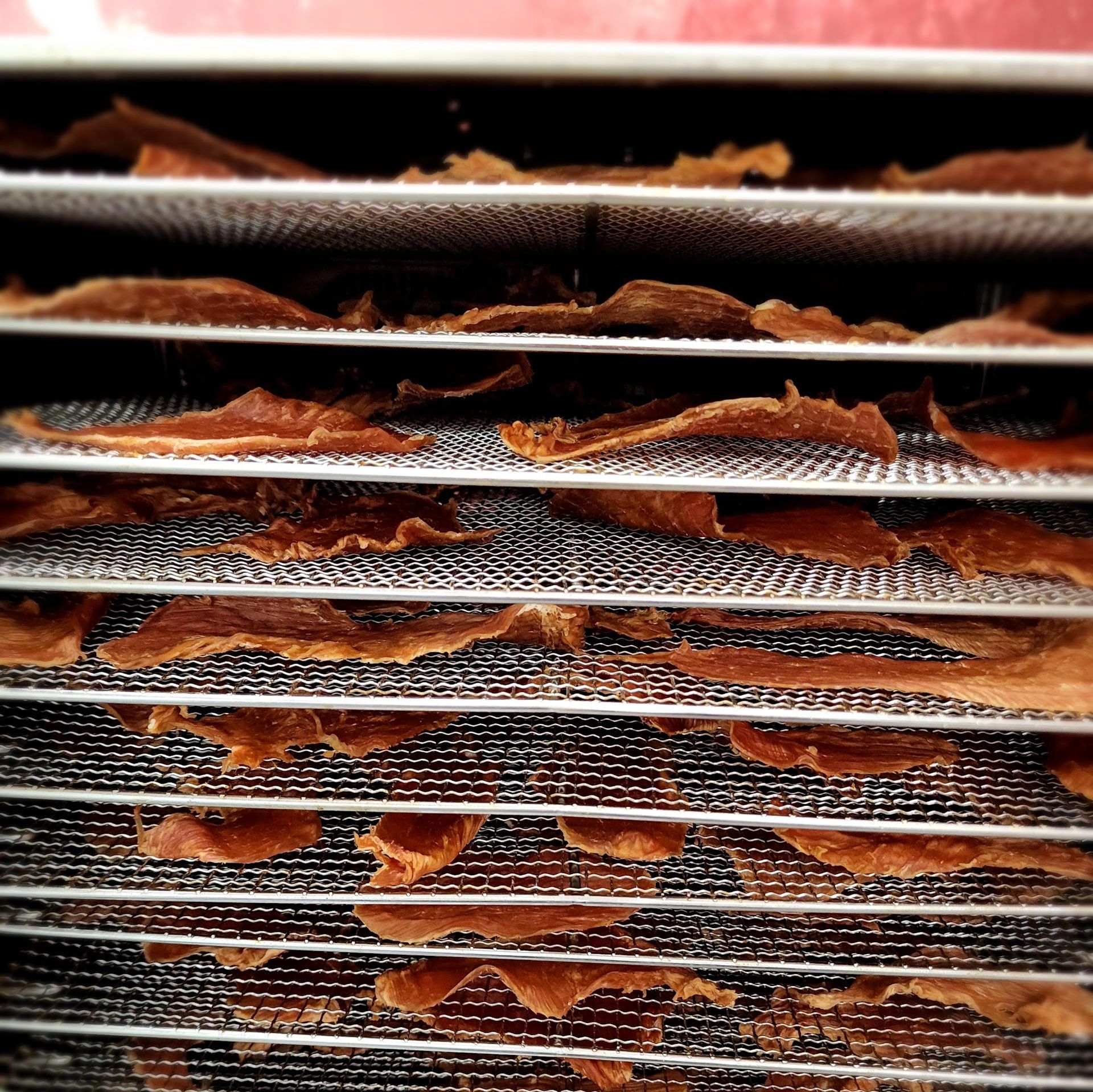 Meat jerky drying on wire racks inside a dehydrator.