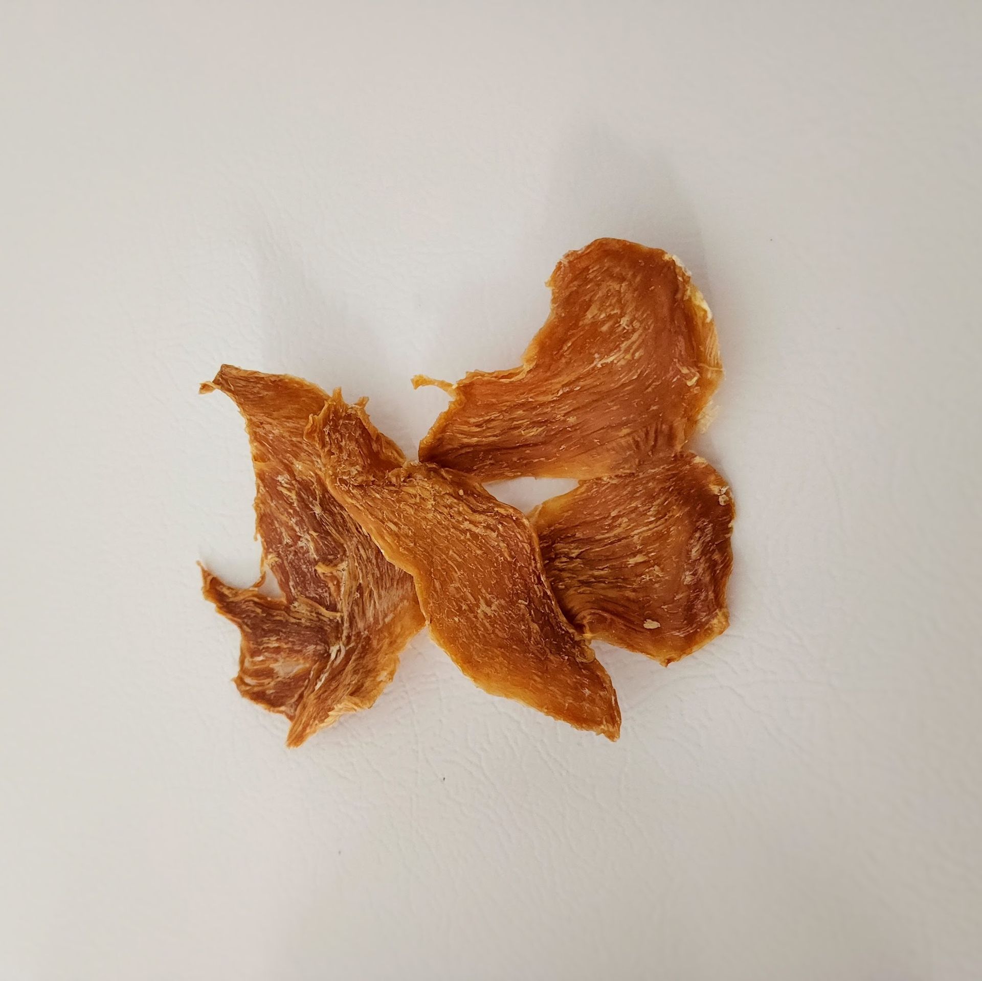 Dried, golden-brown chicken jerky pieces on a white surface.