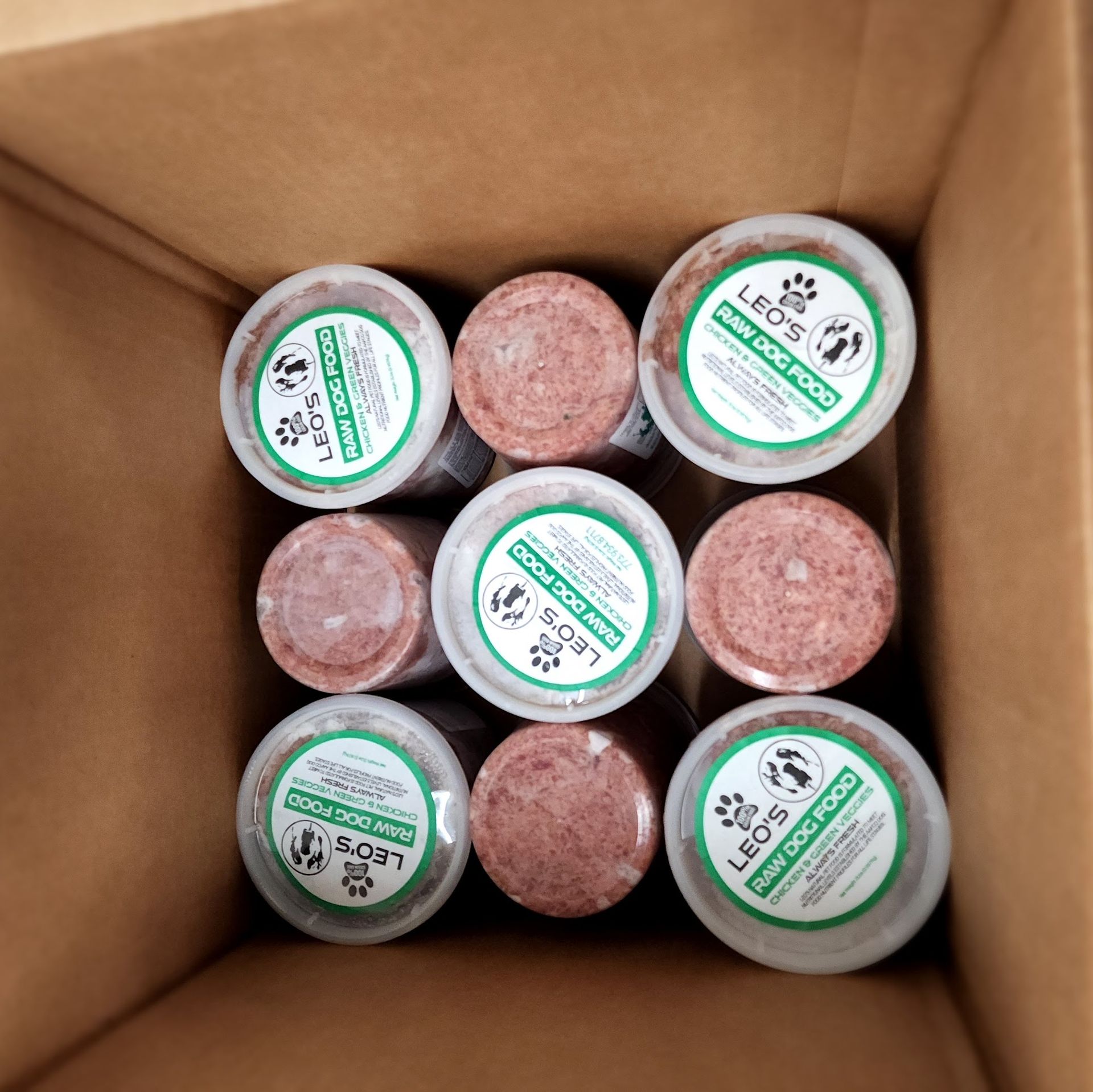 Cardboard box containing nine tubs of dog food with green labels.