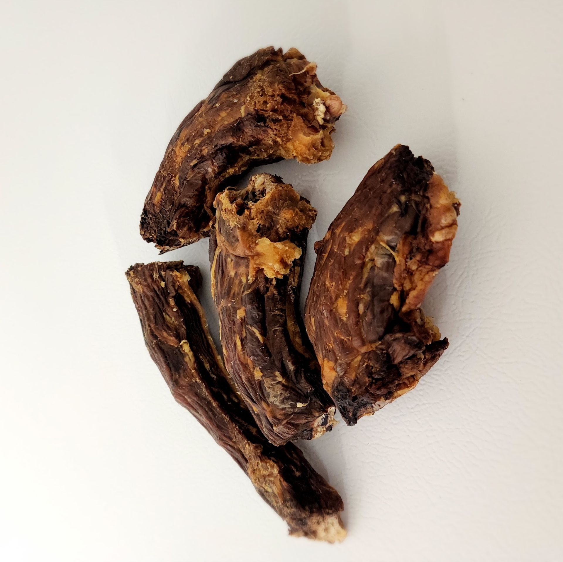 Dried dog treats, dark brown, several pieces, against white background.