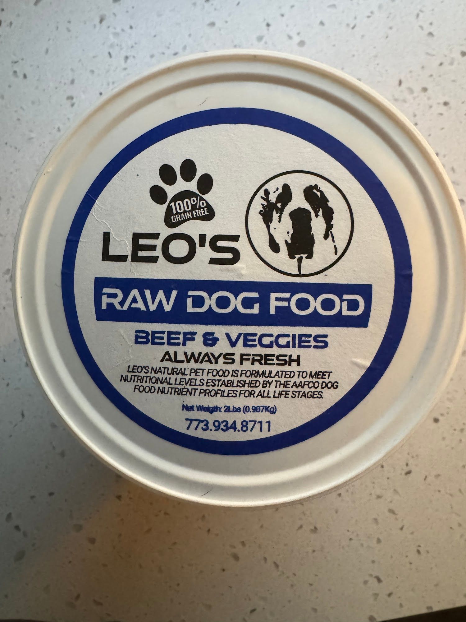 White container of Leo's Raw Dog Food; blue label with paw print, dog silhouette, text: "Beef & Veggies," phone number.