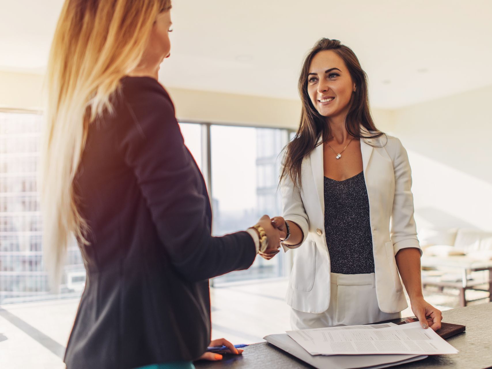 Two women real estate agents are shaking hands in an office.