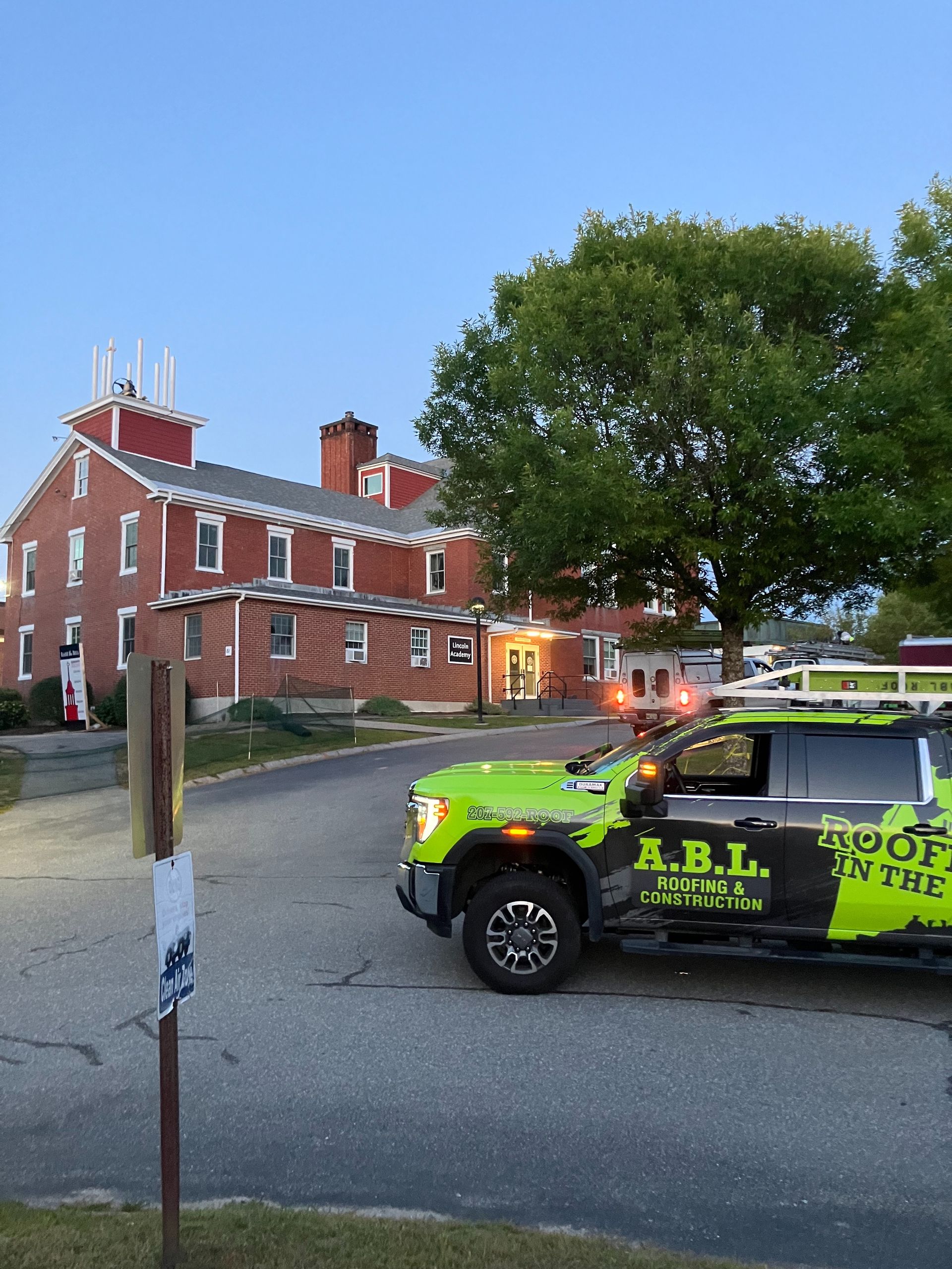 A green a.b.l. truck is parked in front of a brick building