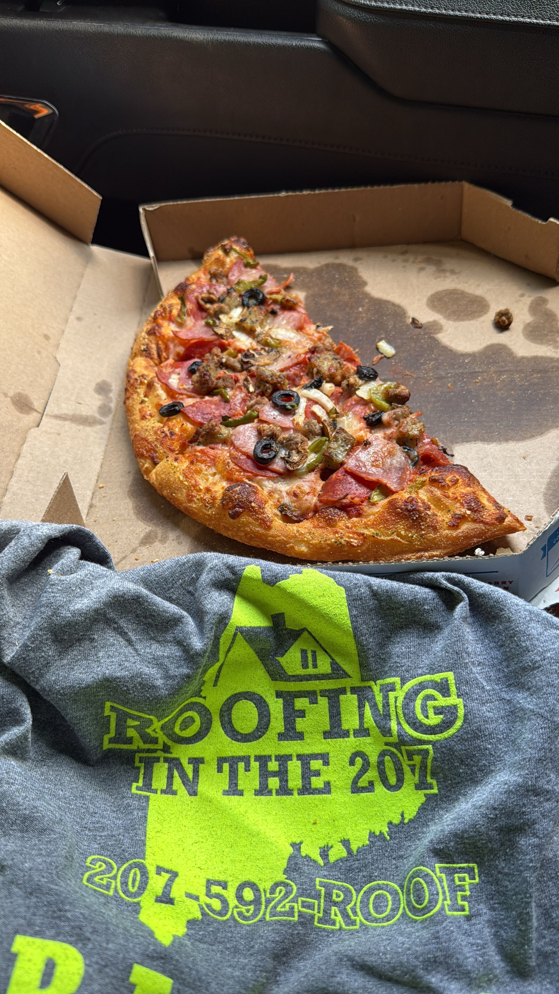 A pizza in a box next to a roofing shirt