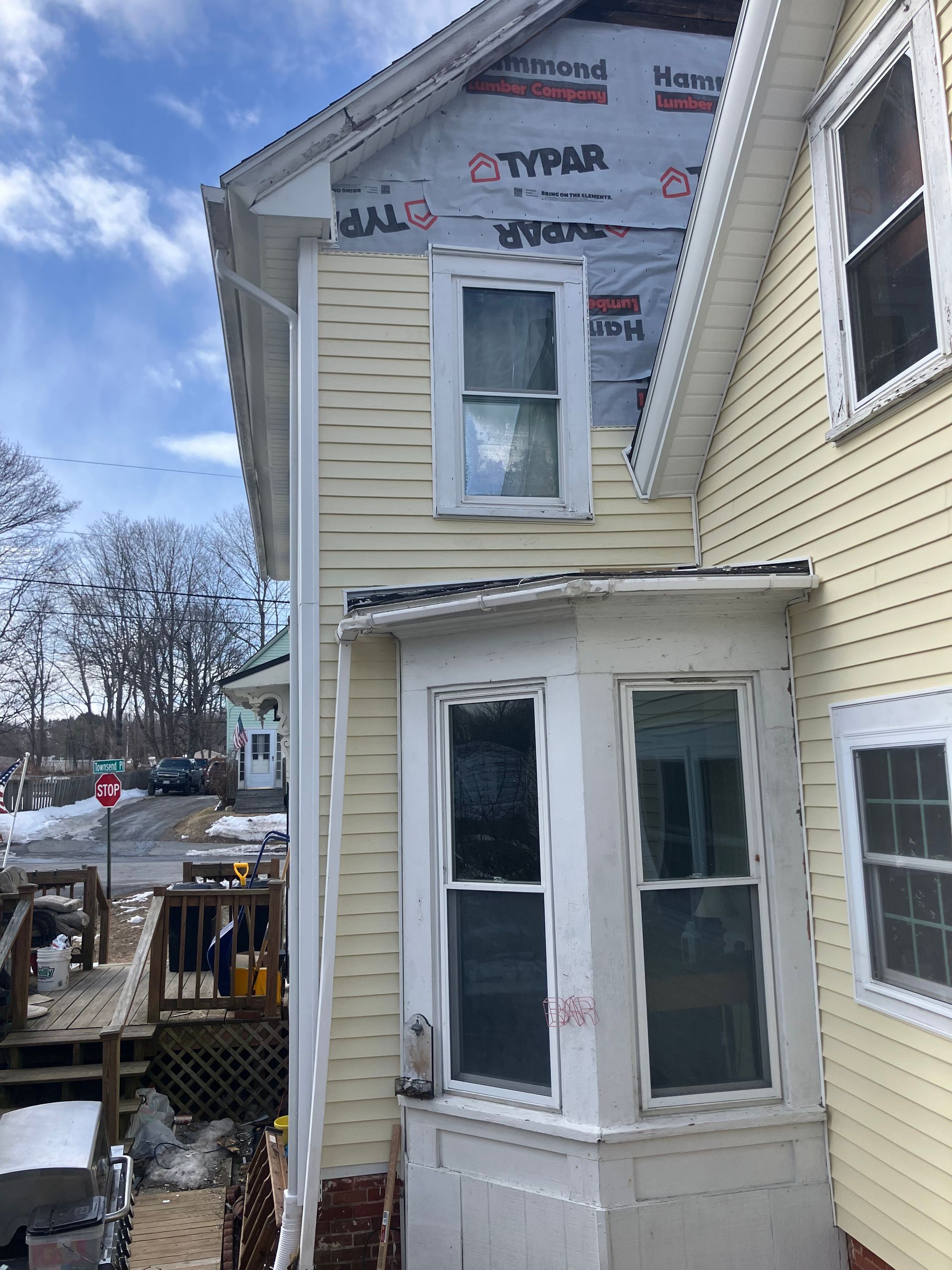 A yellow house with a bay window is being remodeled.