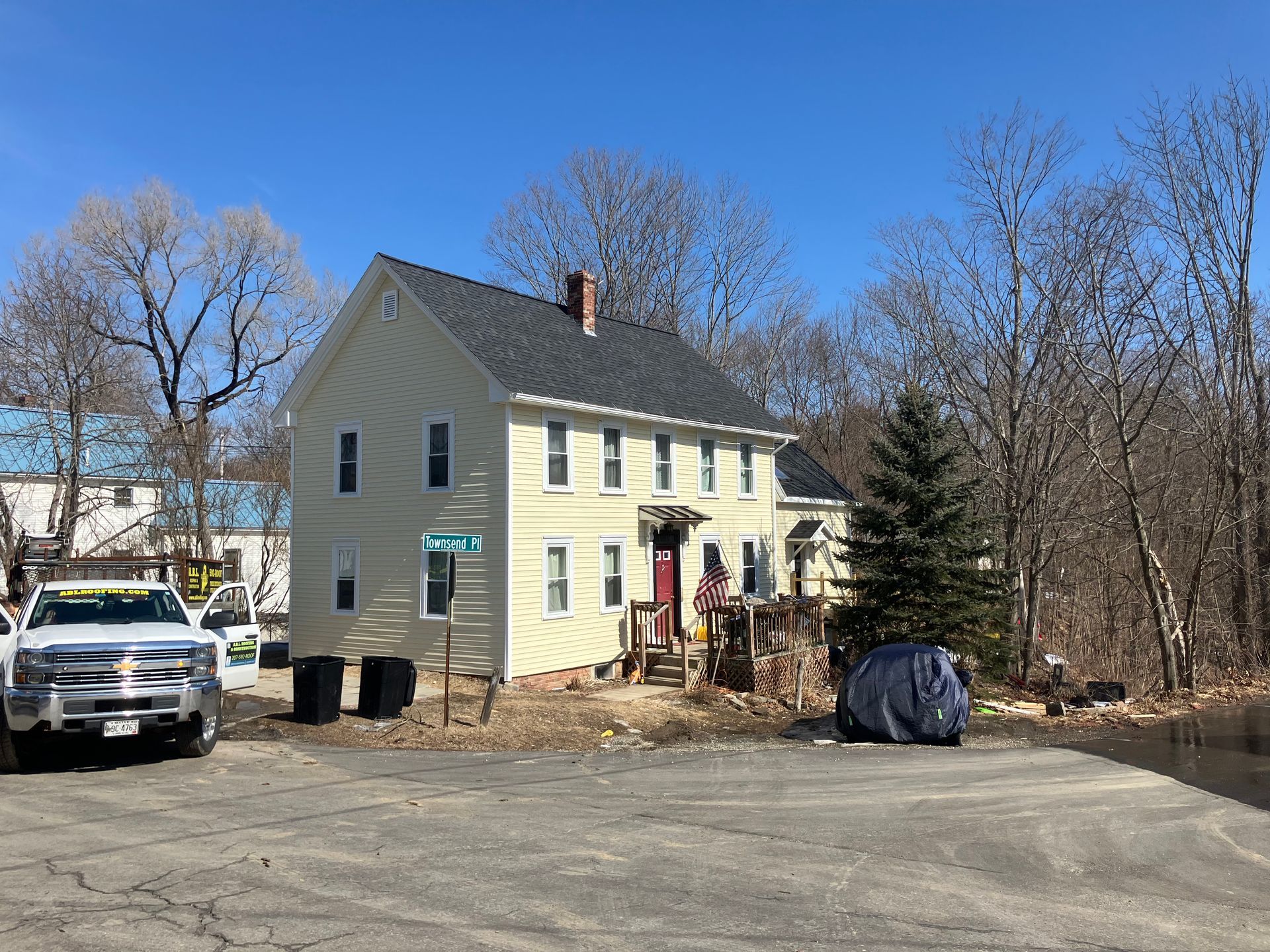 A large white house with a gray roof is surrounded by trees and a parking lot.
