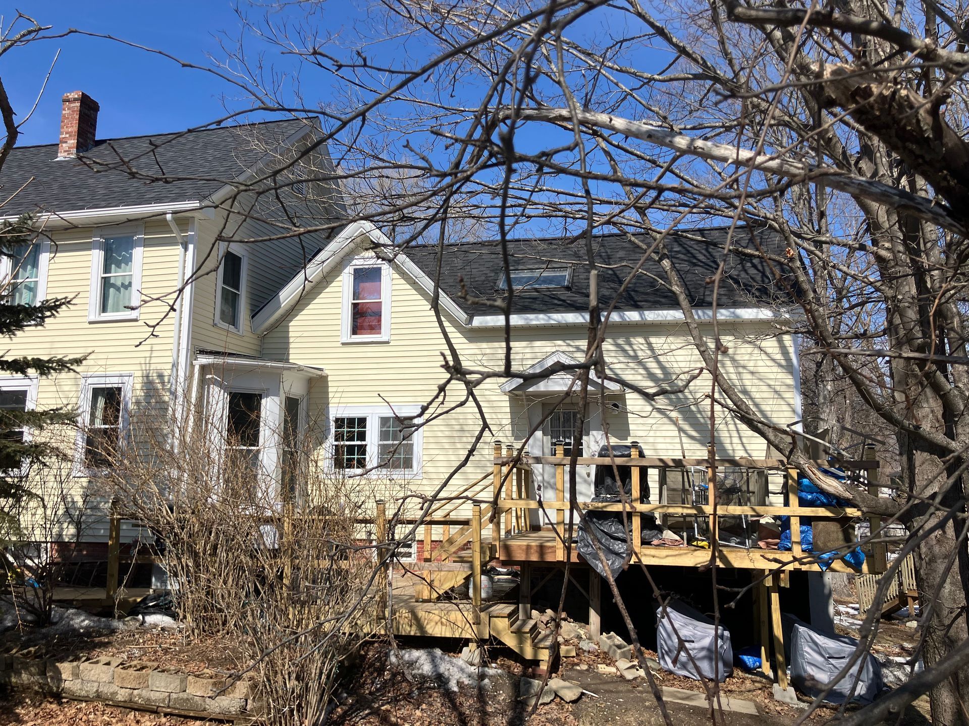 A yellow house with a black roof and a wooden deck in front of it.