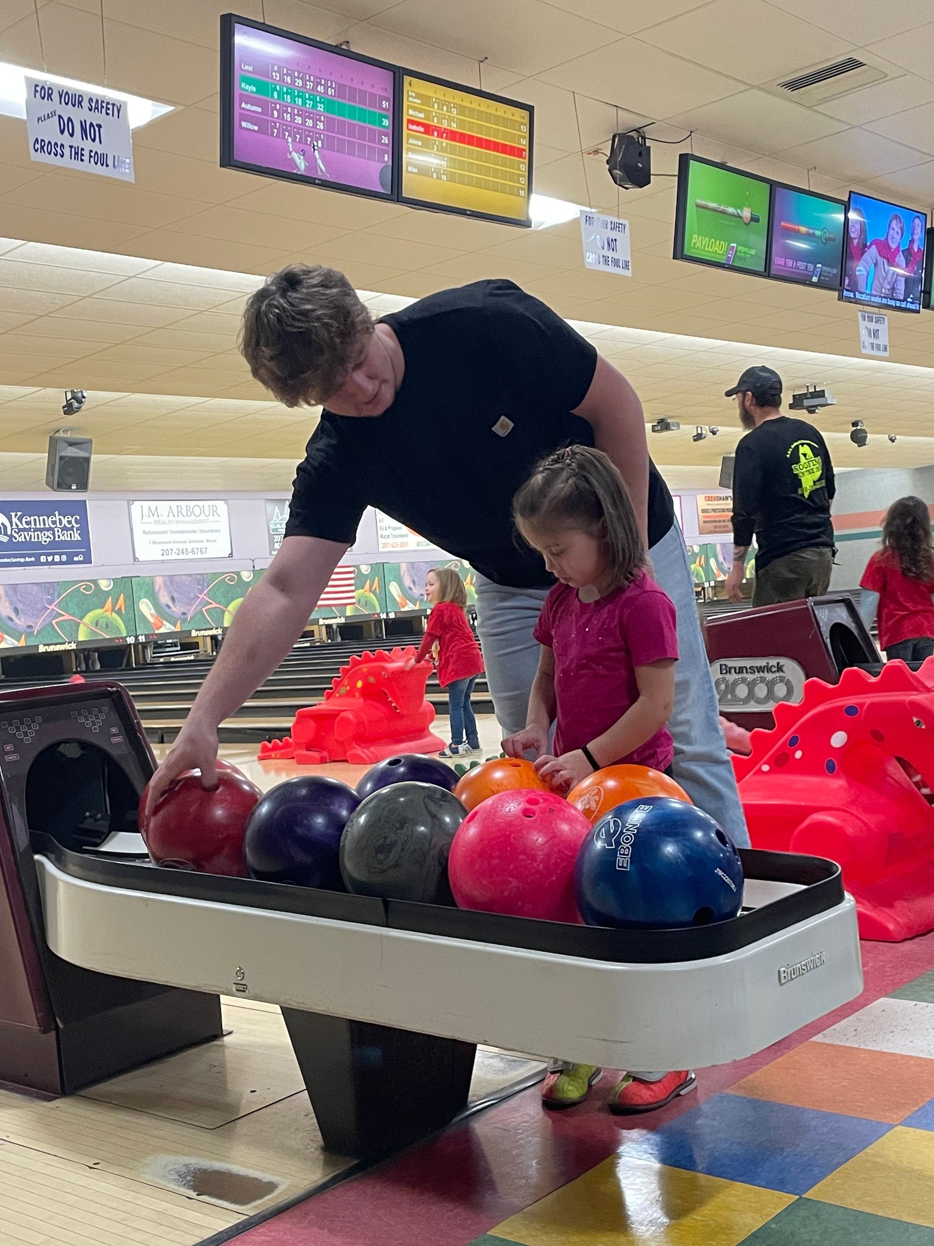 A man and a little girl are playing bowling in a bowling alley.