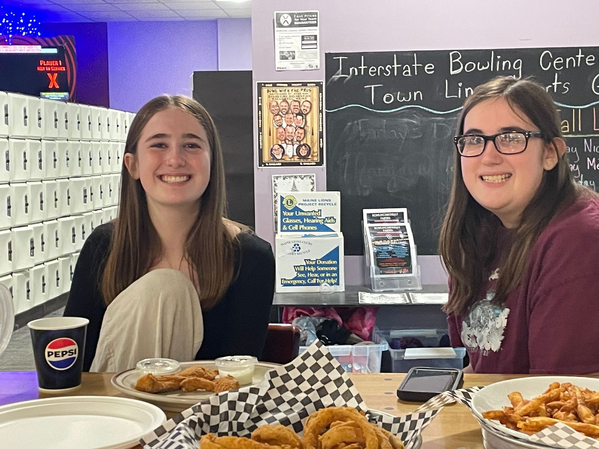 Two girls are sitting at a table with plates of food.