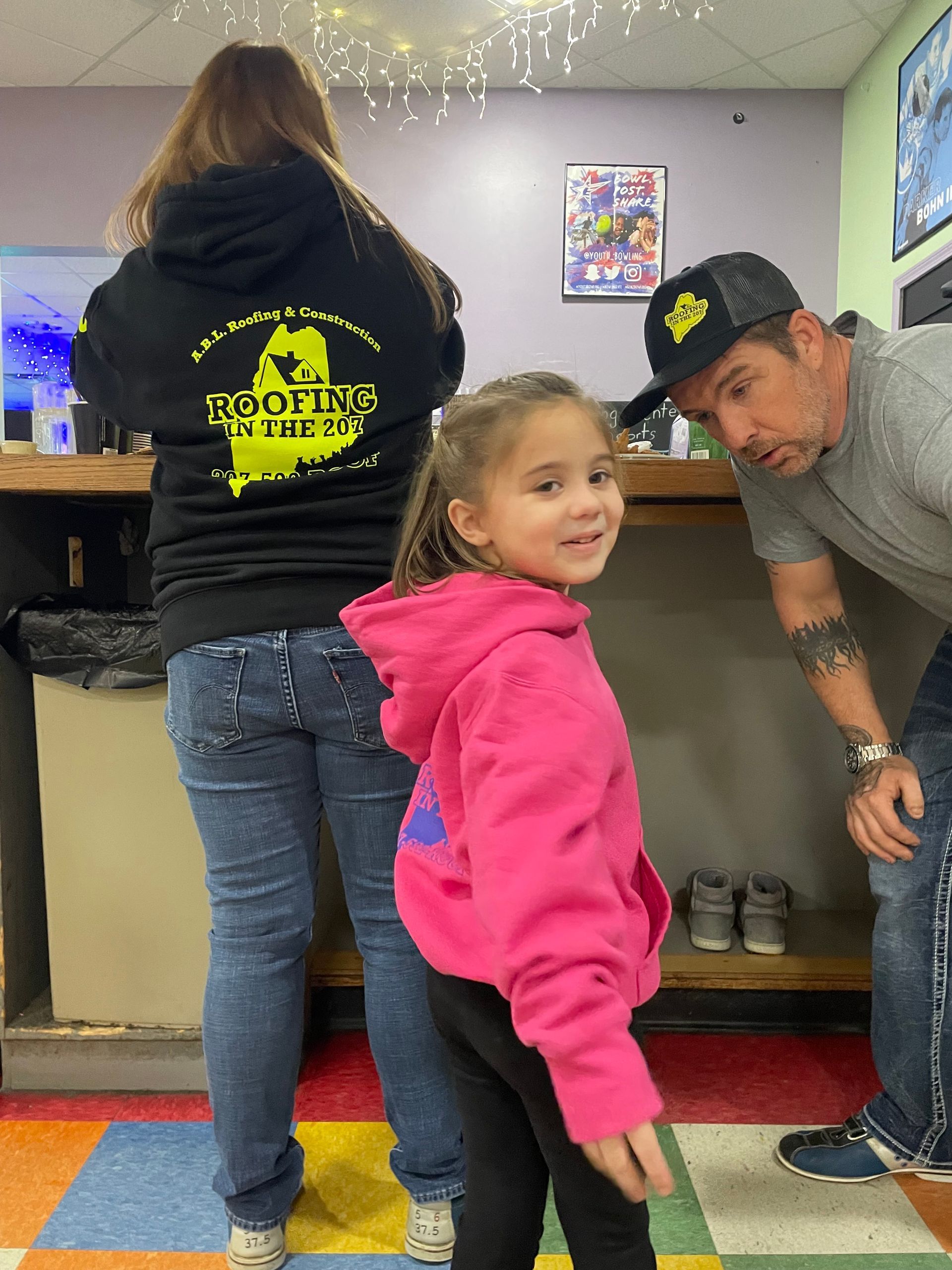 A little girl in a pink hoodie is standing next to a man and woman.
