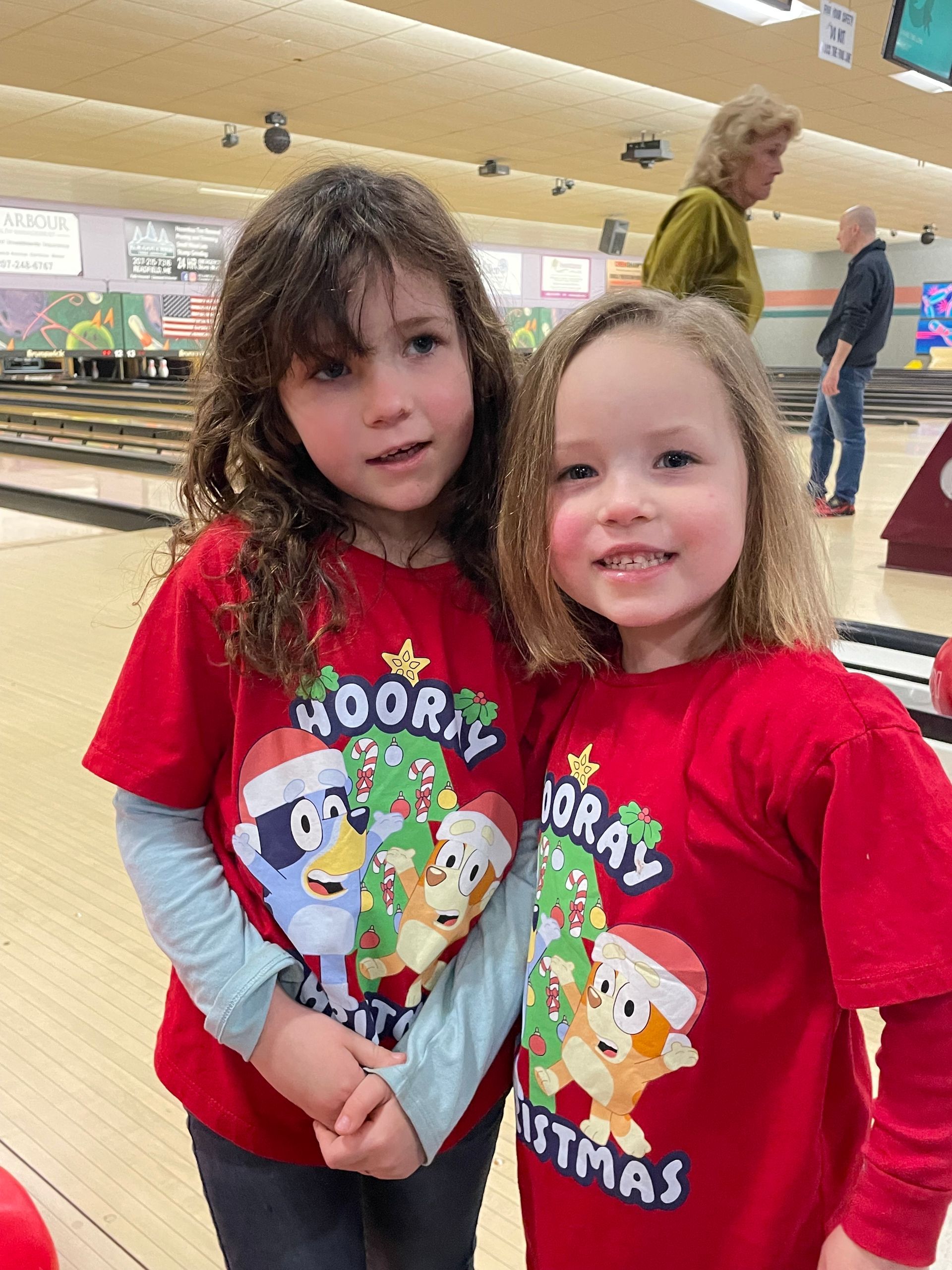 Two little girls are standing next to each other in a bowling alley.