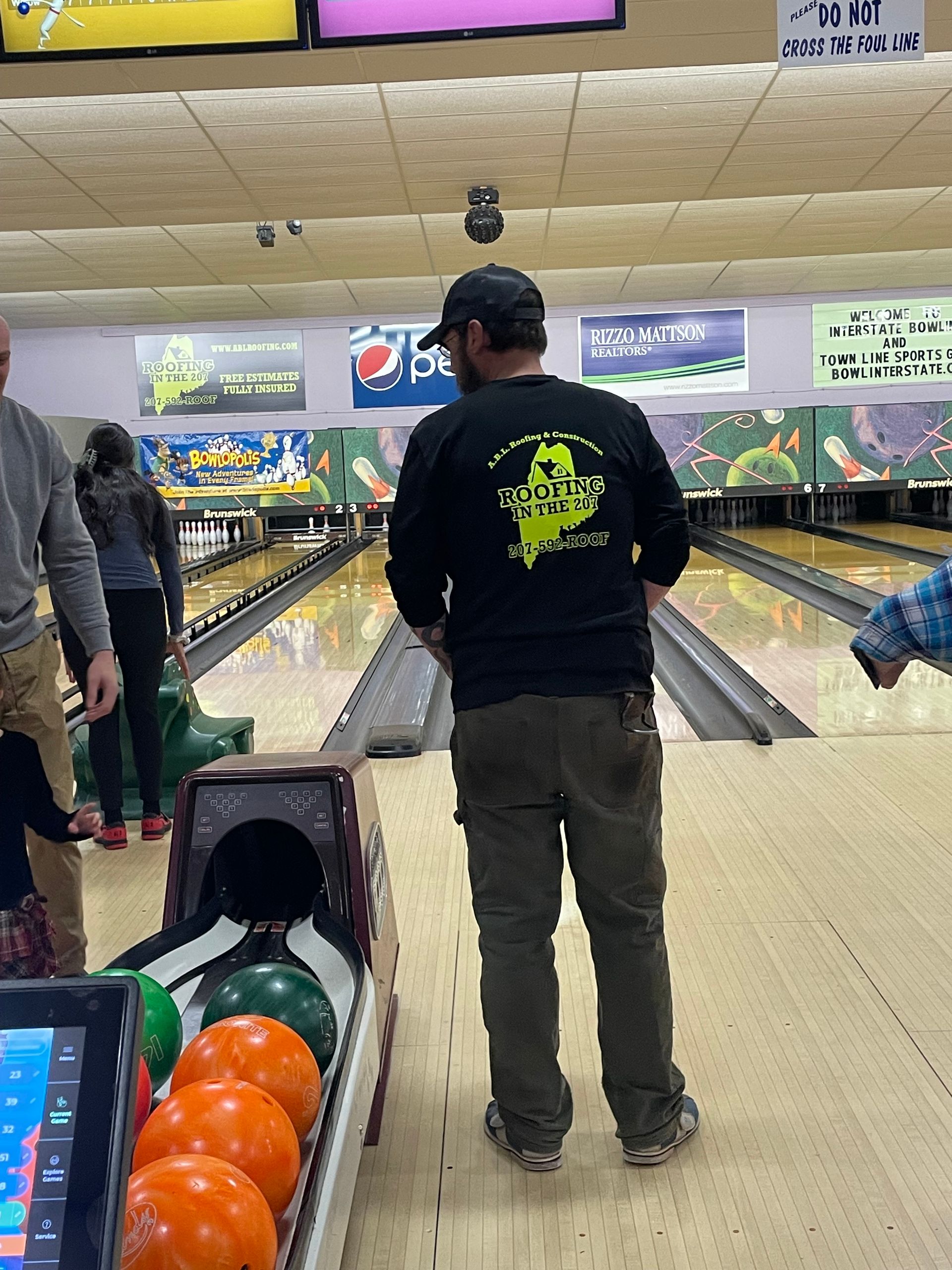 A man wearing a black shirt with a wizard on it is standing in a bowling alley