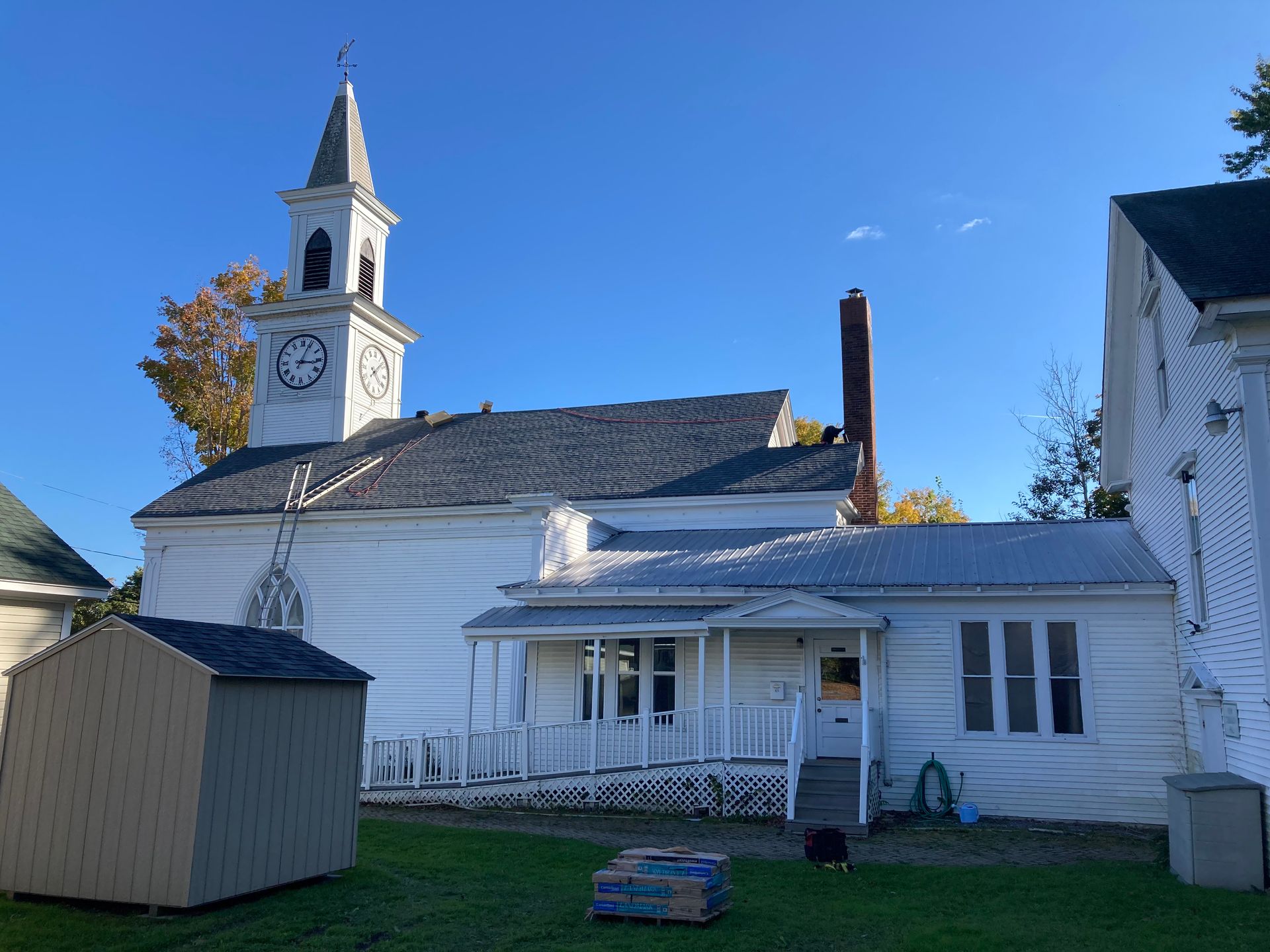 A white house with a clock tower and a shed in front of it.