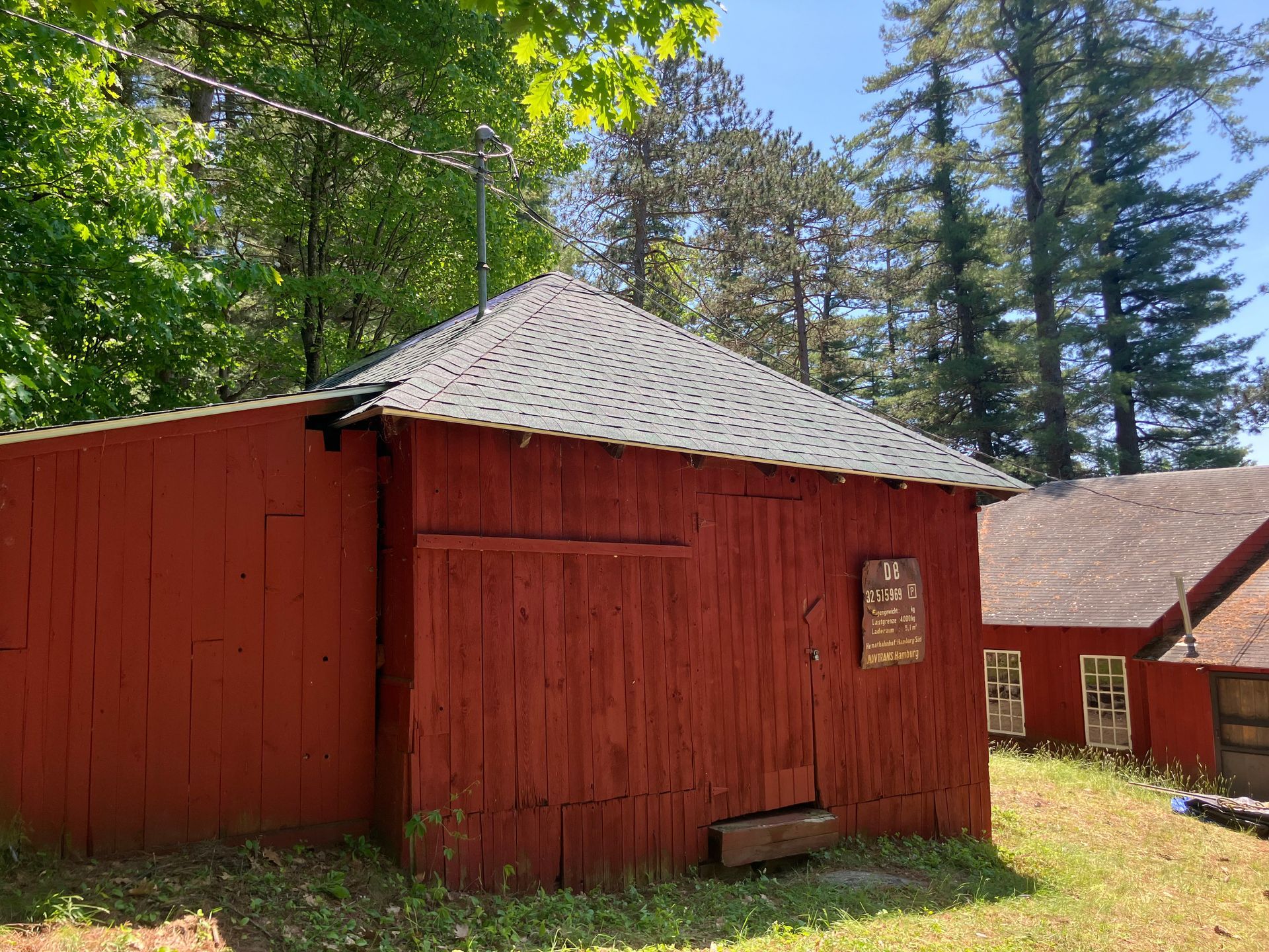 A red barn with a roof is sitting in the middle of a grassy field.