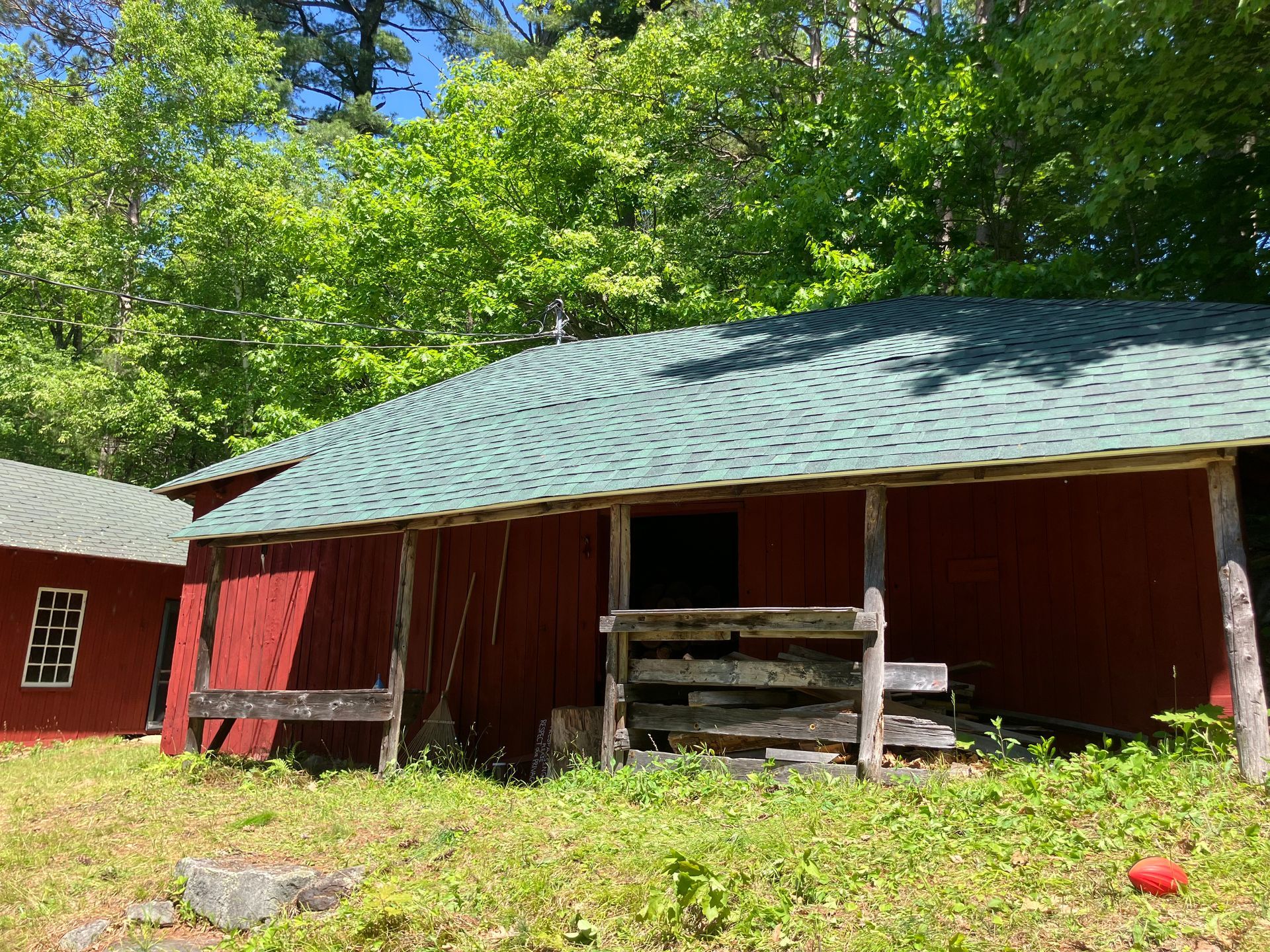 A red barn with a green roof is surrounded by trees.