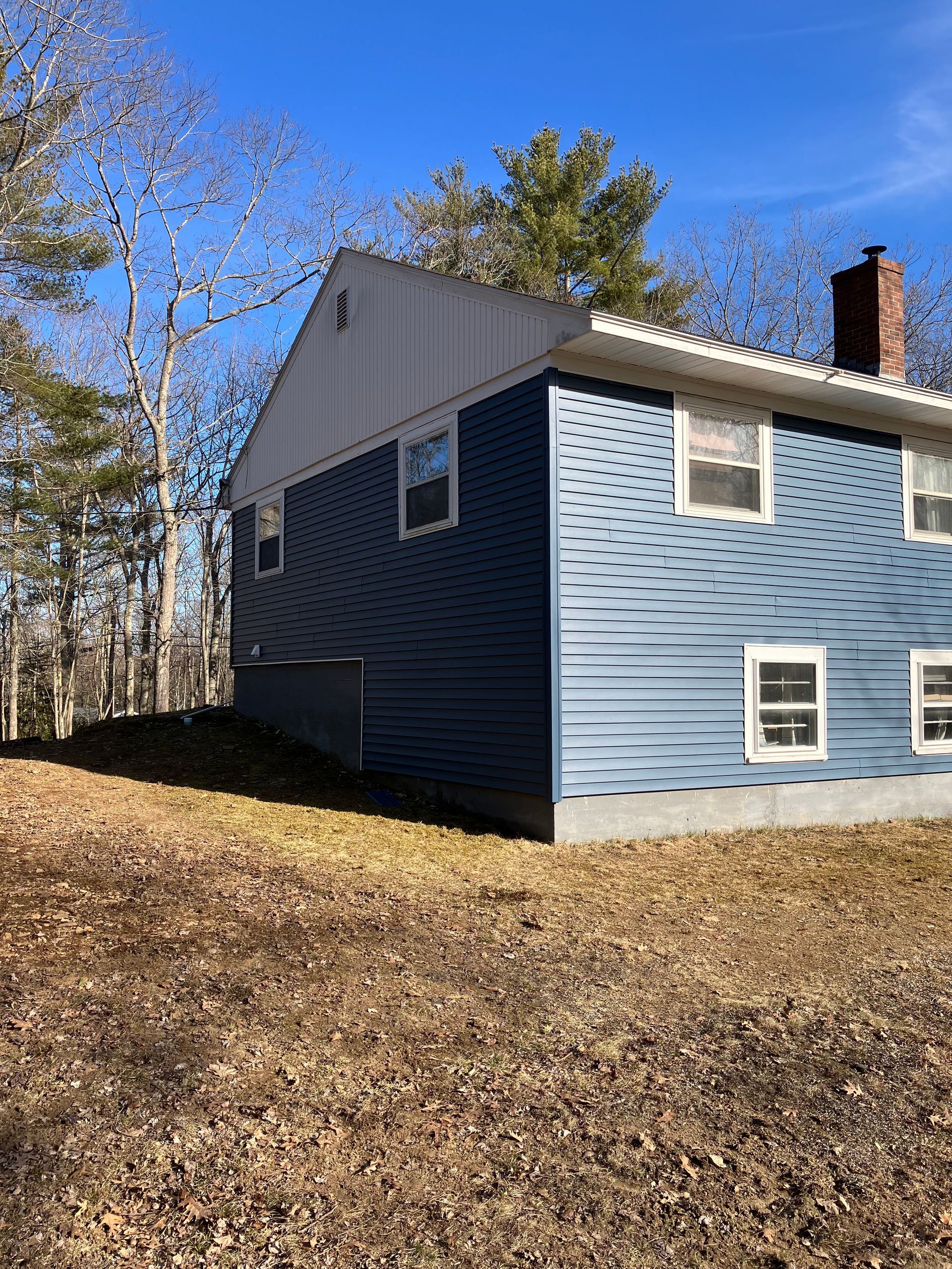 A blue house with a white roof is sitting on top of a grassy hill.