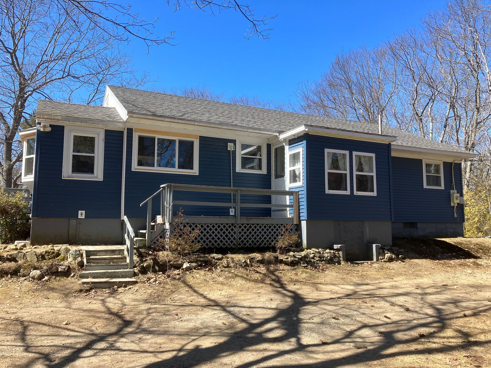 A blue house with a gray roof is sitting in the middle of a dirt field.