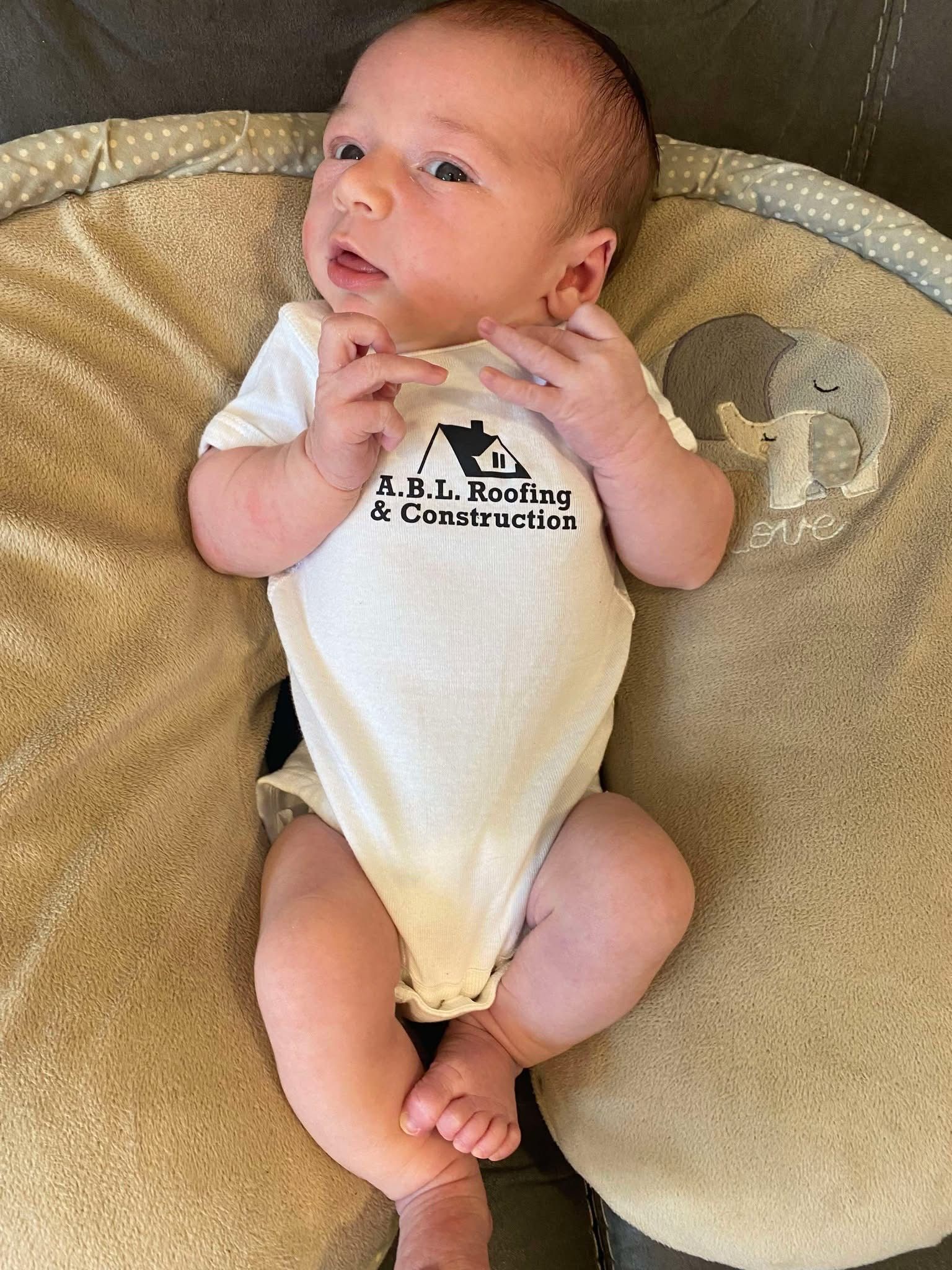 A baby in a white onesie is laying on a pillow.