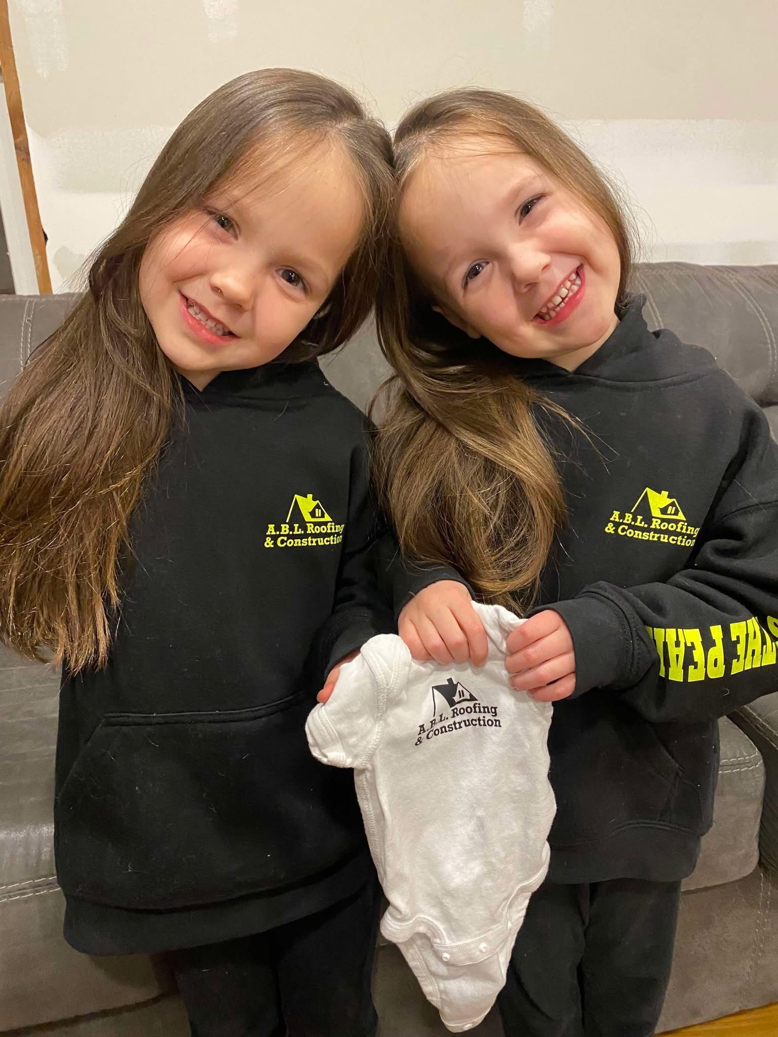 Two little girls are standing next to each other holding a baby onesie.