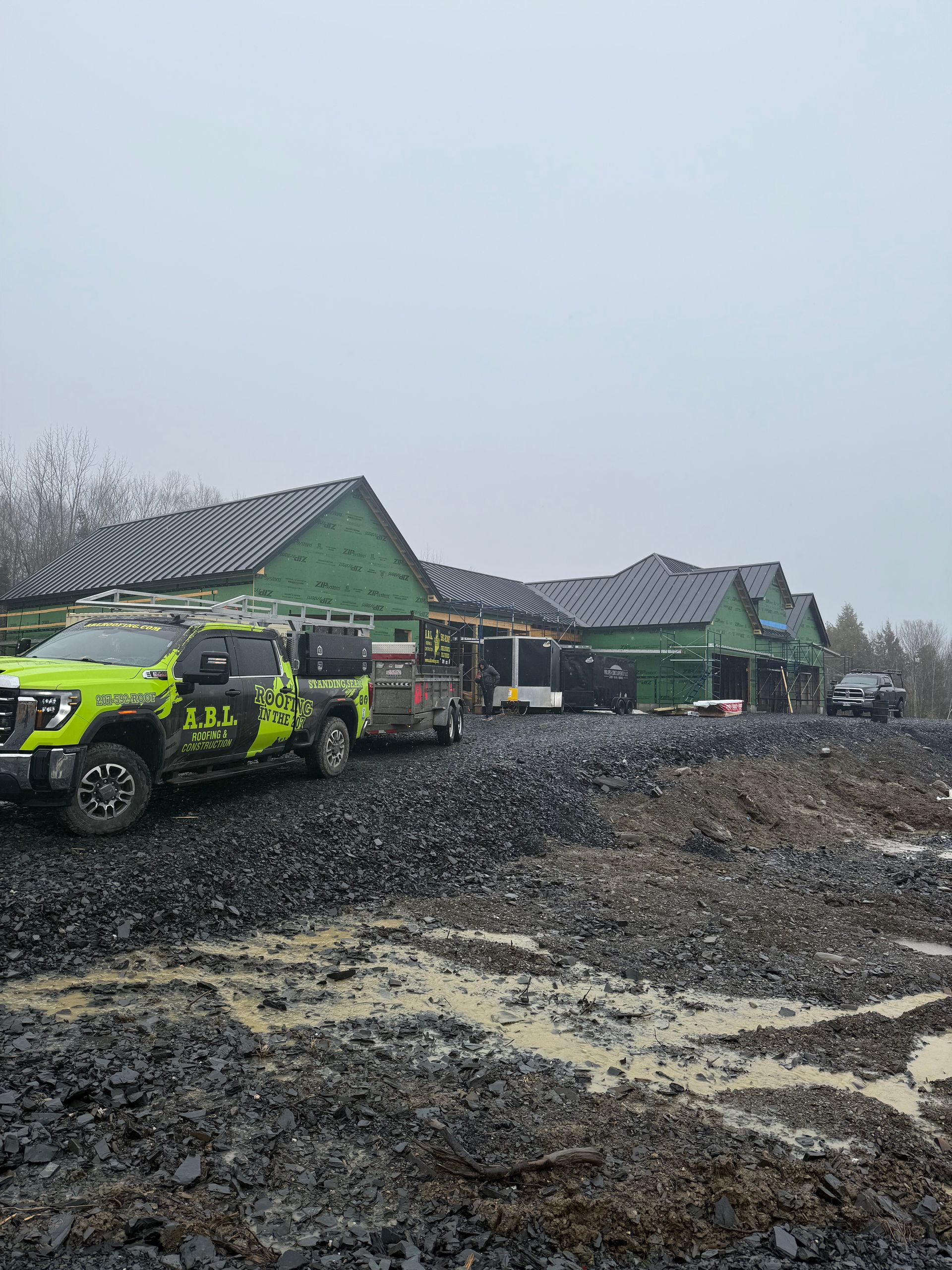 A yellow truck is parked in a muddy field in front of a building under construction.
