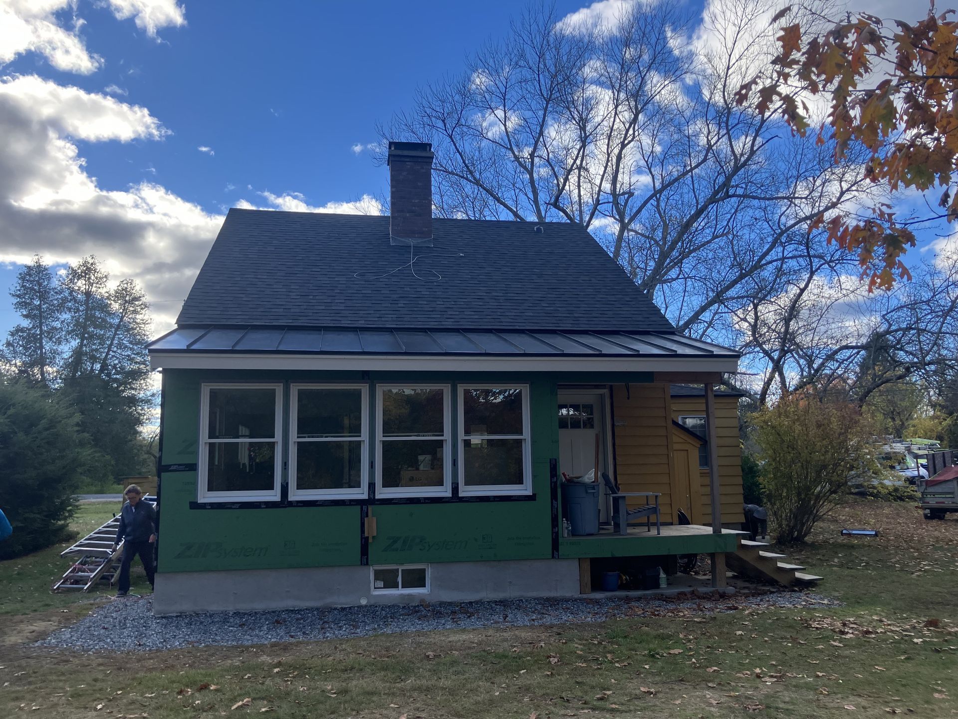 Small house under construction; green siding, dark roof, chimney, porch. Person nearby.