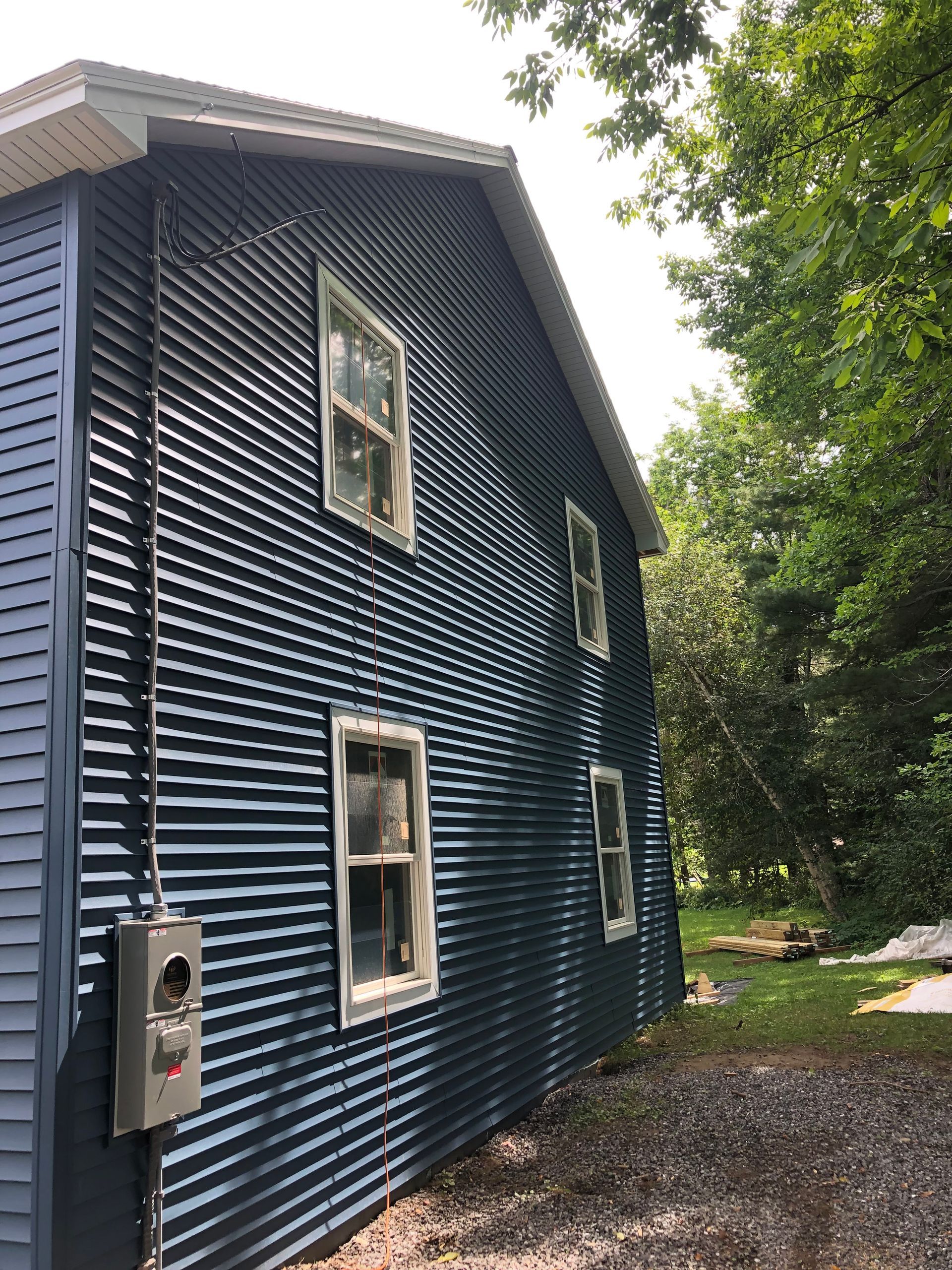 A blue house with a corrugated metal siding and white windows.