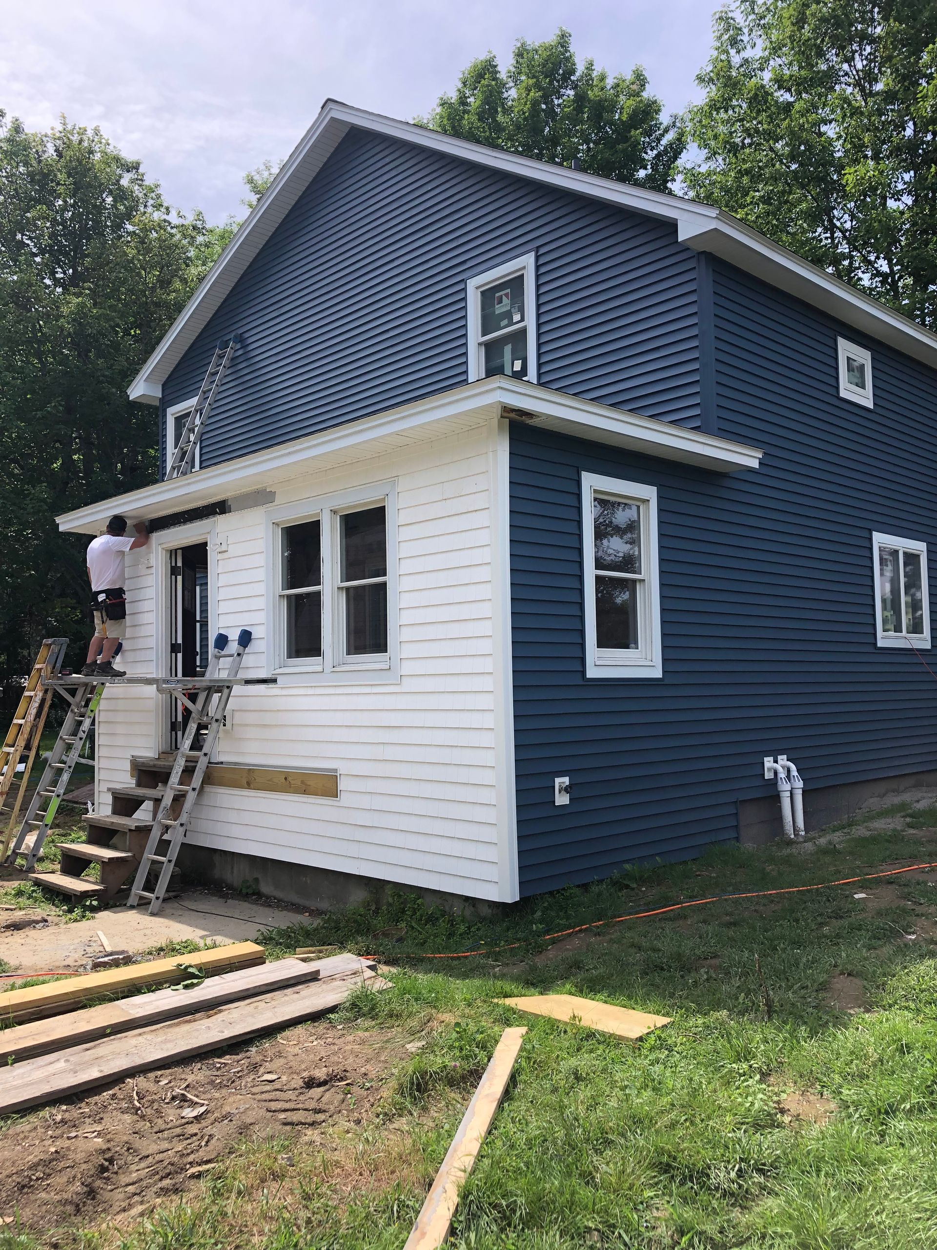 A blue and white house is being painted by a man on a ladder.