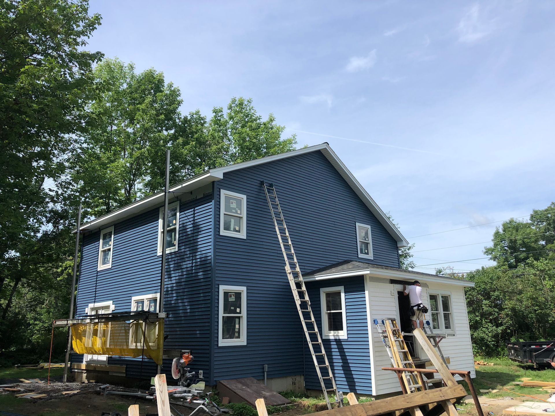 A blue house is being painted with a ladder.