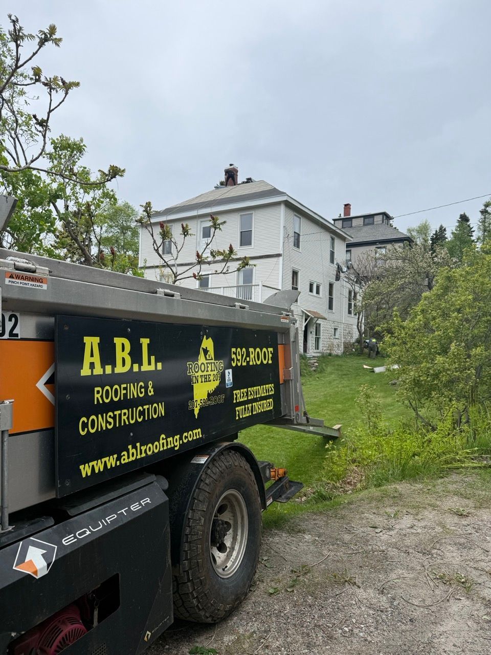 A roofing and construction truck is parked in front of a house.