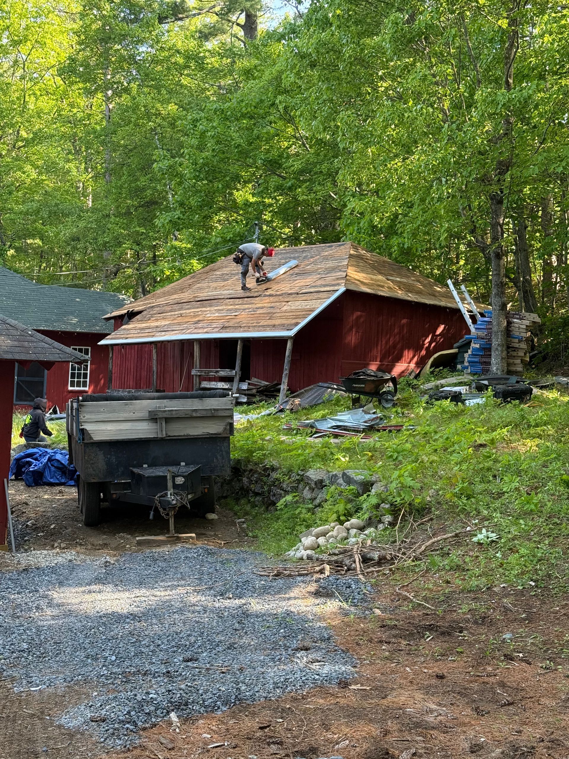 A man is working on the roof of a red barn.