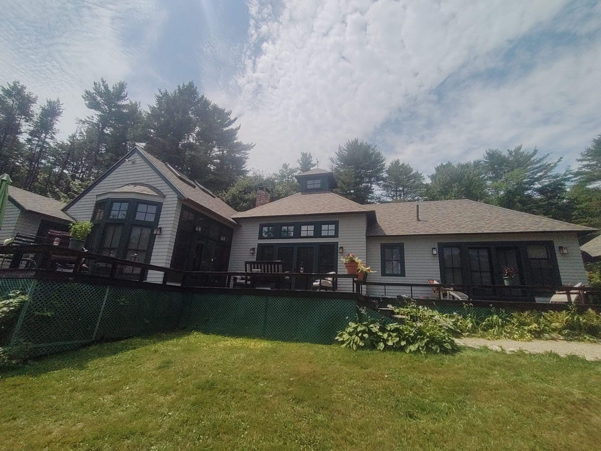 A white house with a brown roof is surrounded by trees on a sunny day.