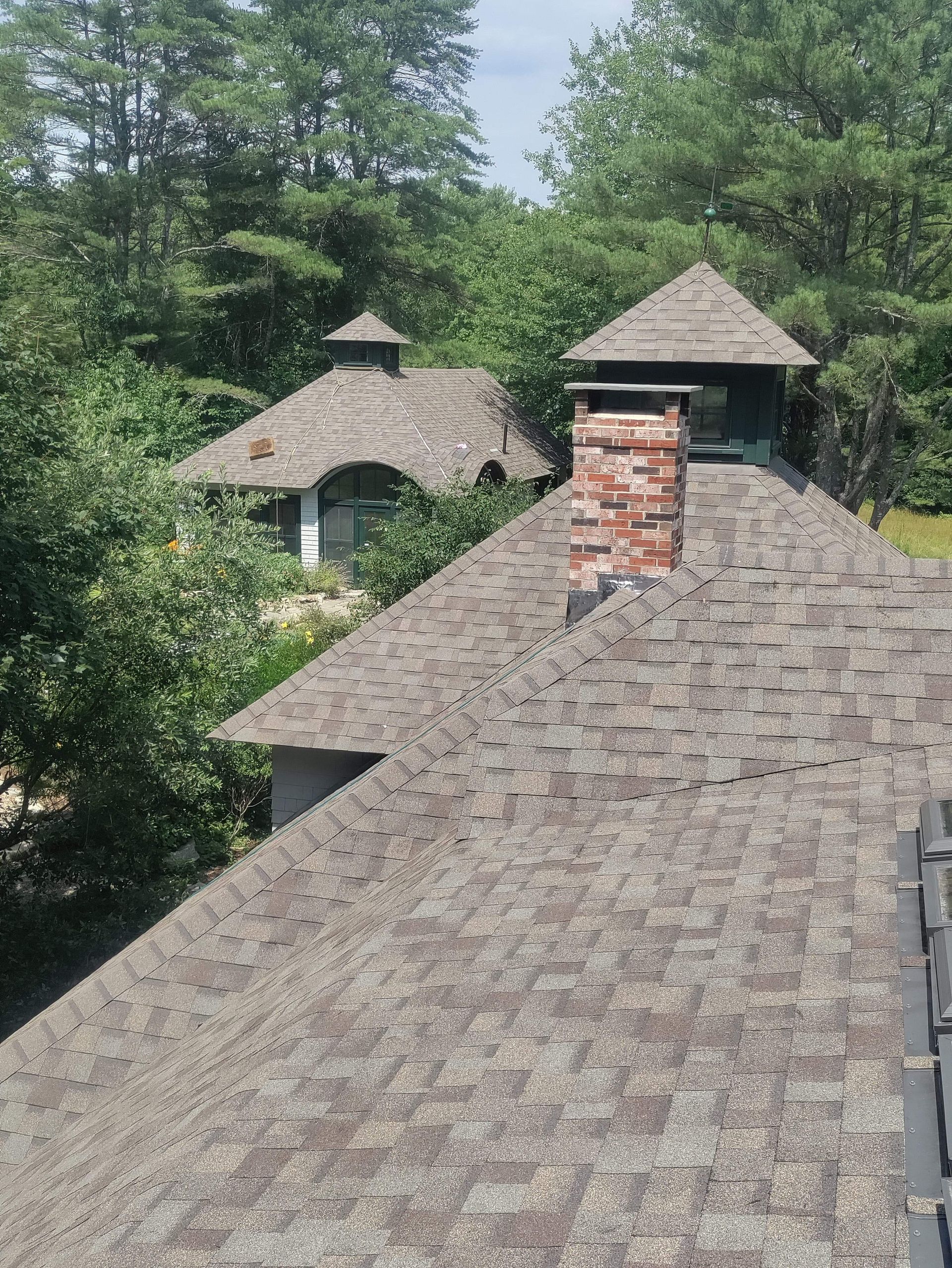 A roof with a chimney on it is surrounded by trees.