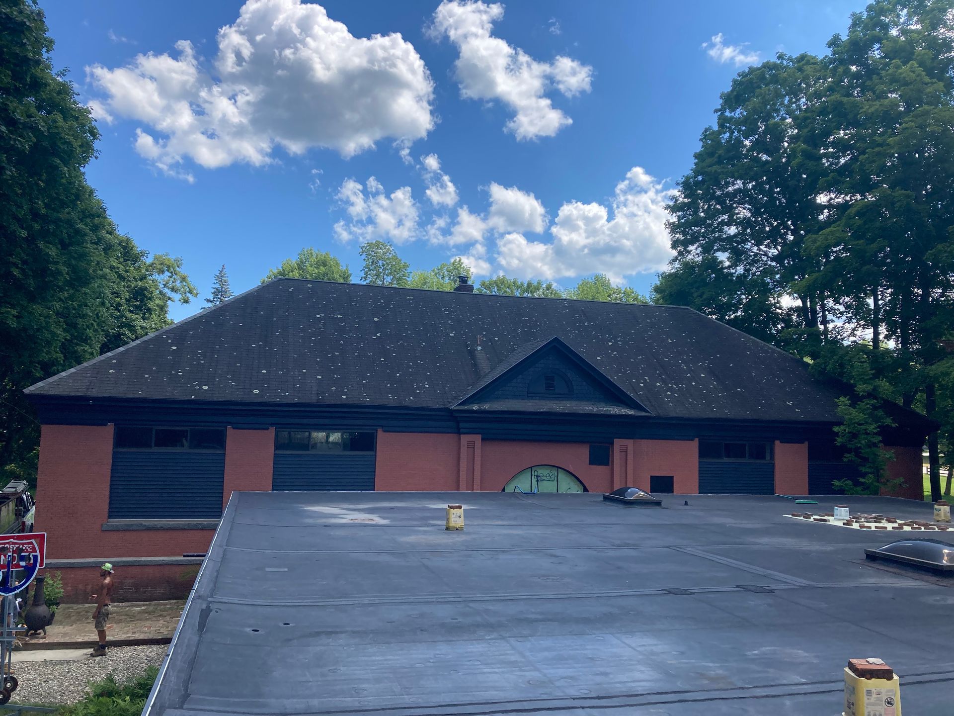 A large brick building with a black roof and trees in the background