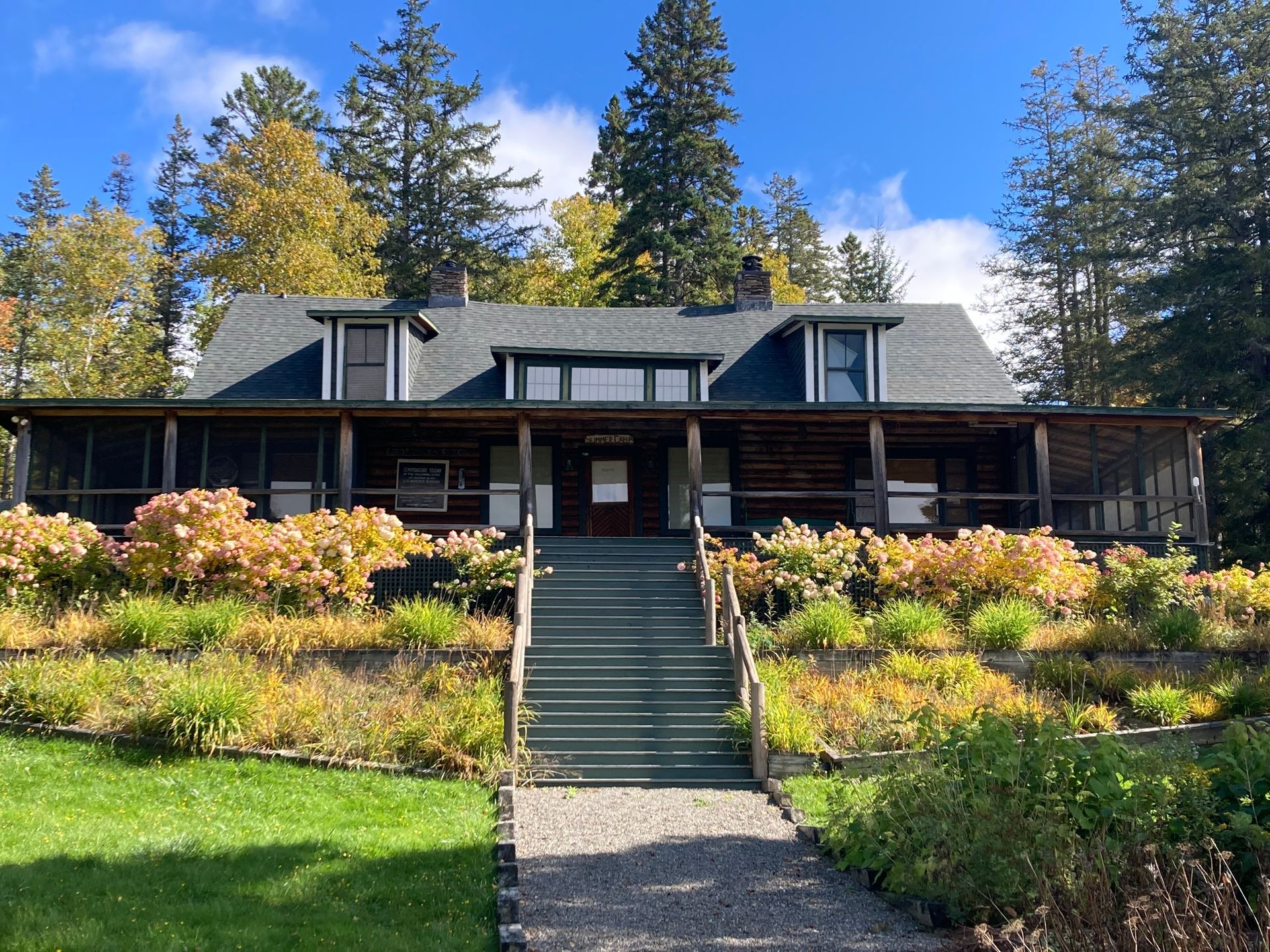 A large house with stairs leading up to it is surrounded by trees.